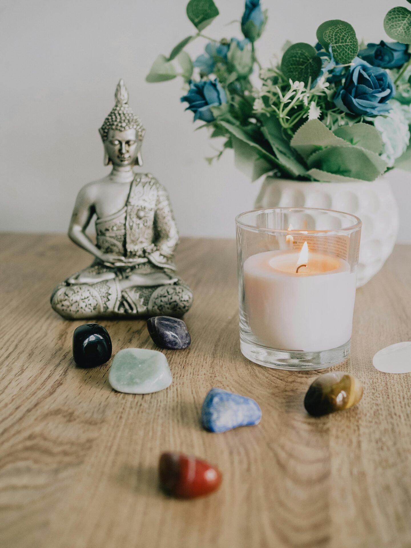 Buddha-Statue, brennende Kerze, Kristalle und 7 Chakren-Akzente auf einem Holztisch.