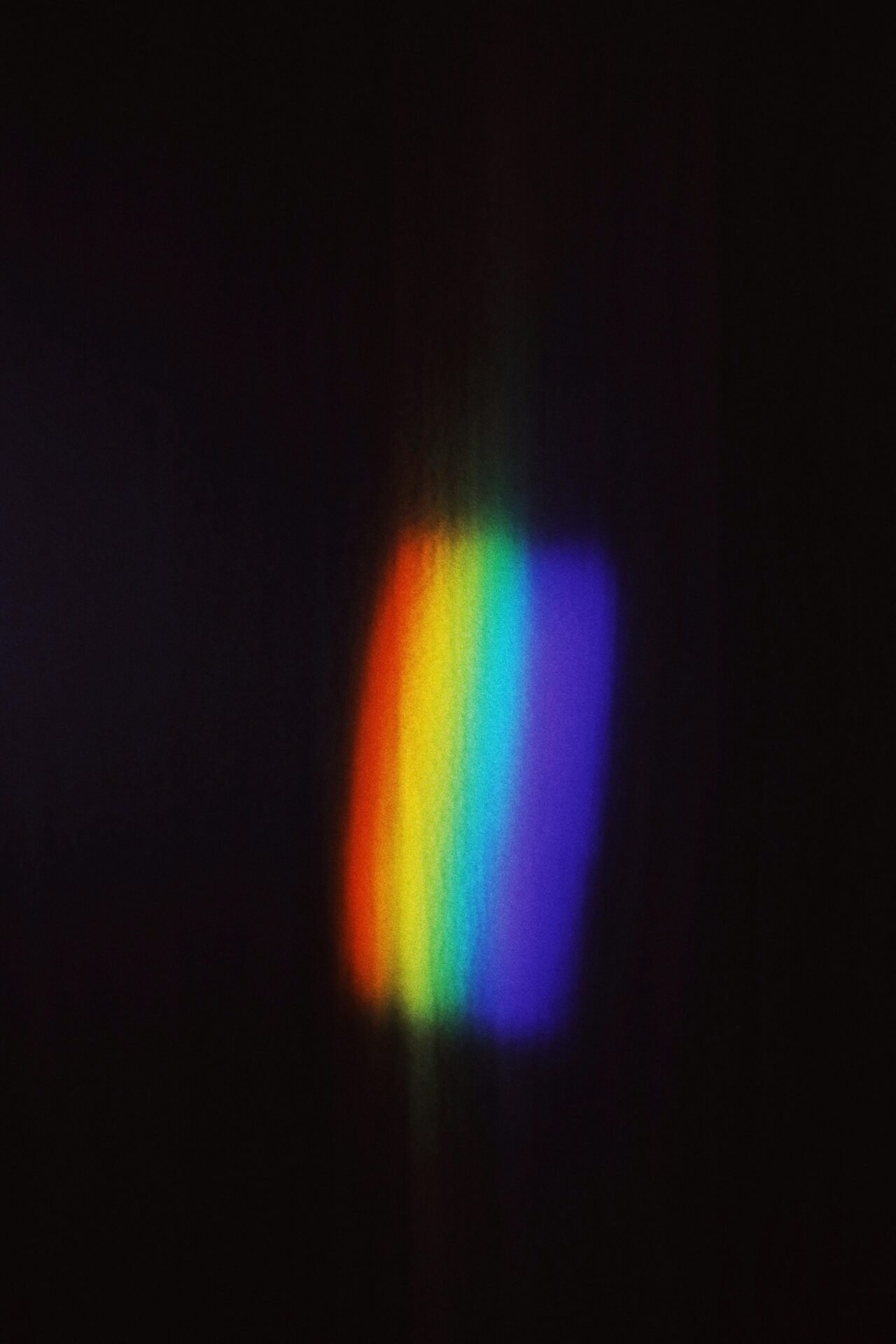 Ein vertikales Spektrum von Regenbogenfarben leuchtet wie die 7 Chakren vor einem dunklen Hintergrund.
