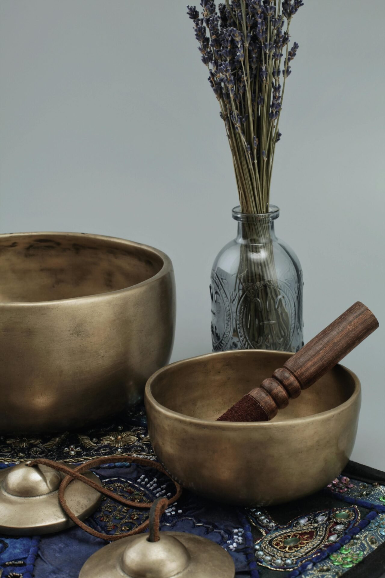 Messingklangschalen für 7 Chakren, ein Holzschlägel und getrockneter Lavendel auf gemustertem Stoff.