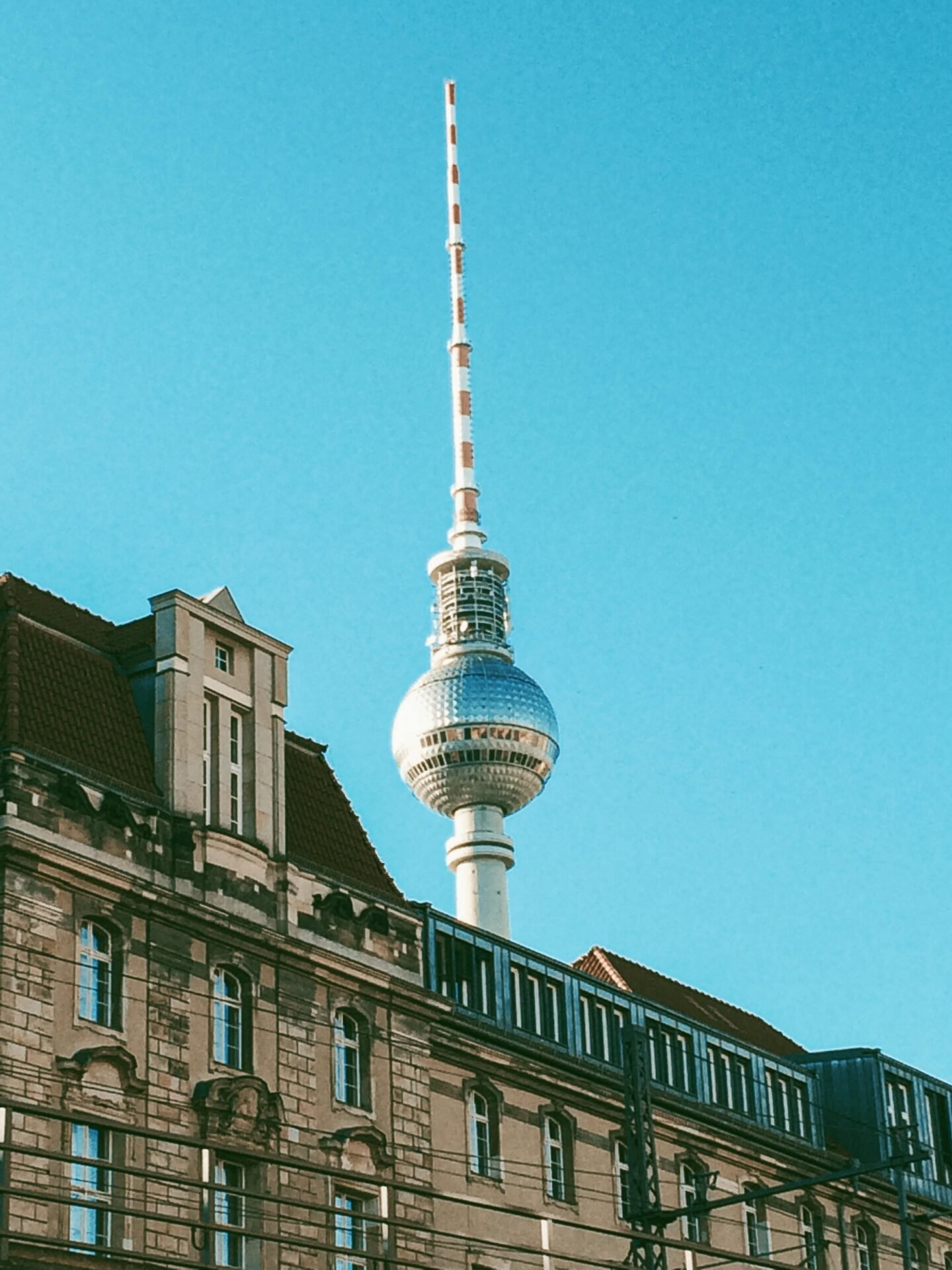 Der Berliner Fernsehturm, eine berliner Sehenswürdigkeit, erhebt sich unter freiem Himmel über einem Altbau.