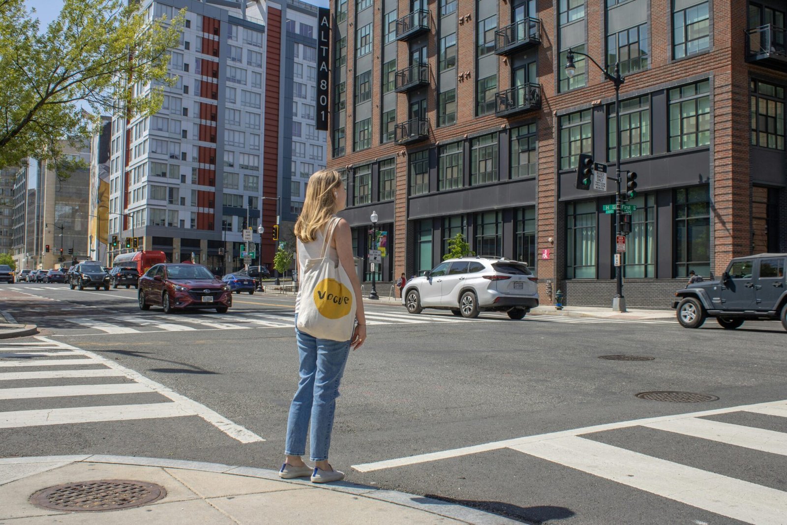 Eine Frau mit einer gelben Einkaufstasche wartet an einem Zebrastreifen in der Stadt und träumt von einer Arbeit in den USA.