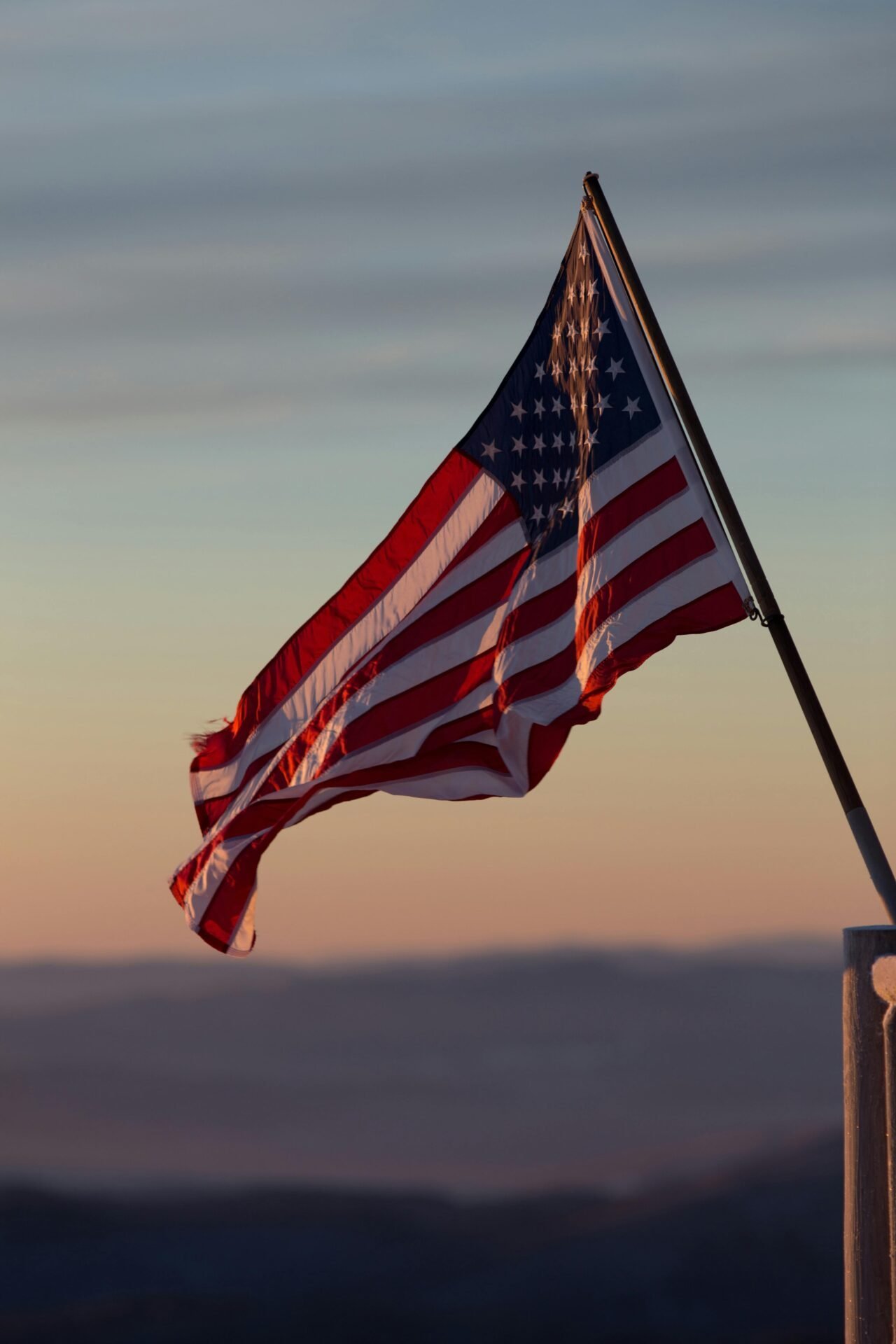 Vor einem pastellfarbenen Sonnenuntergangshimmel weht eine verwitterte amerikanische Flagge, die die Arbeit in den USA symbolisiert.