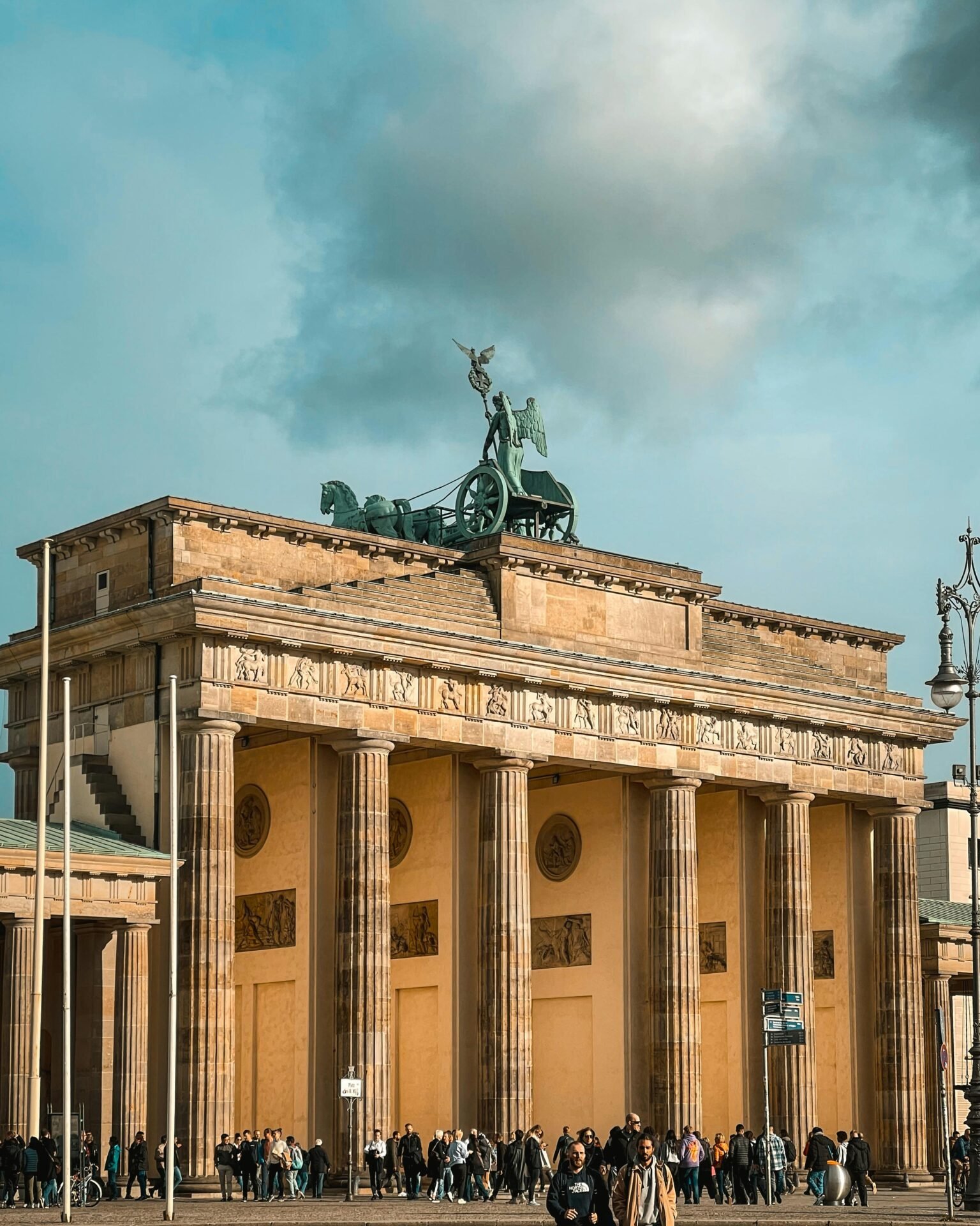 Das Brandenburger Tor in Berlin, eine der besten Sehenswürdigkeiten Berlins, mit Menschenmassen und einem bewölkten Himmel darüber.