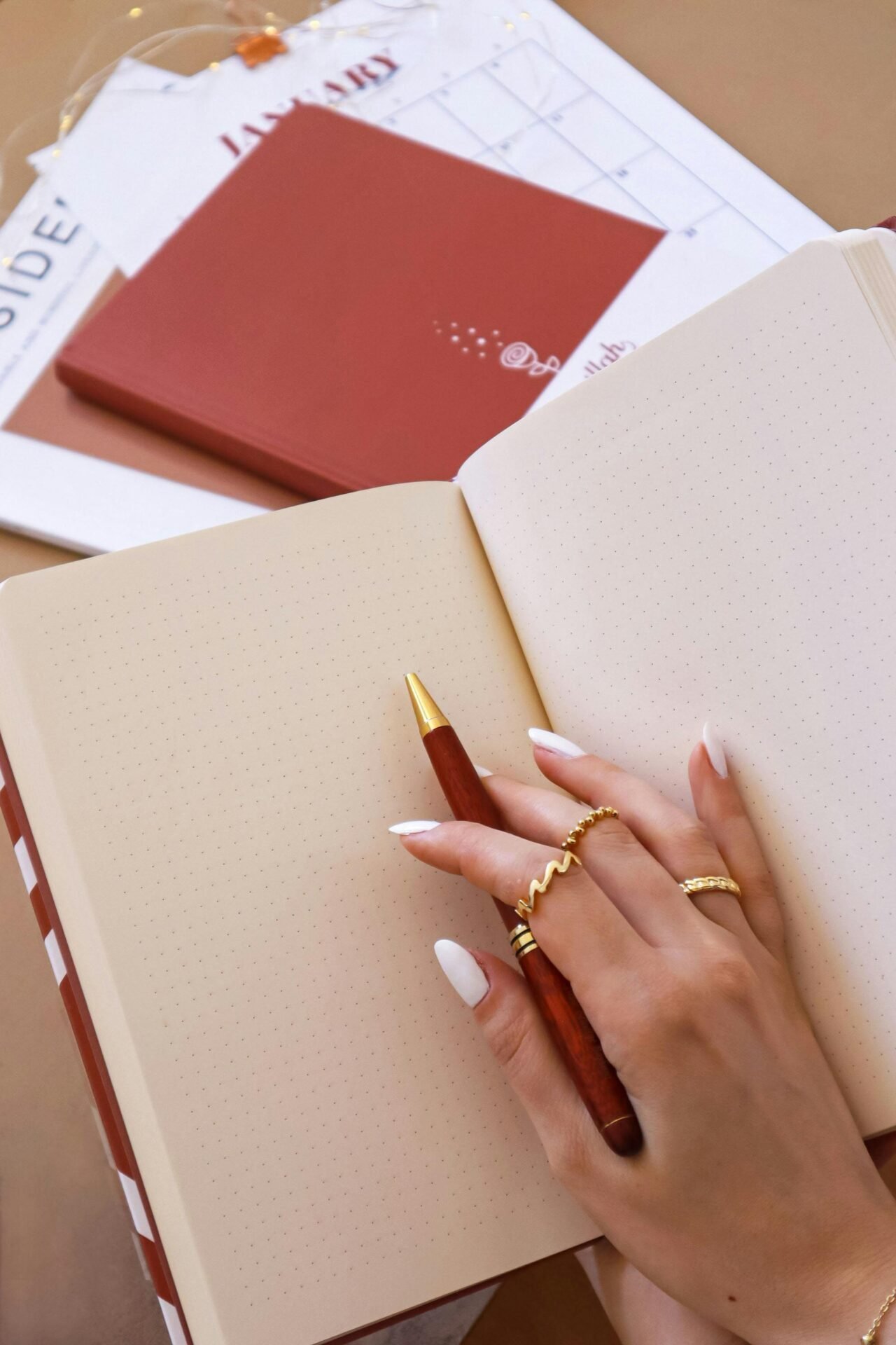 Eine Hand mit Ringen hält einen Stift über ein offenes gepunktetes Notizbuch, bereit für Notizen zur Geschäftsmentalität.