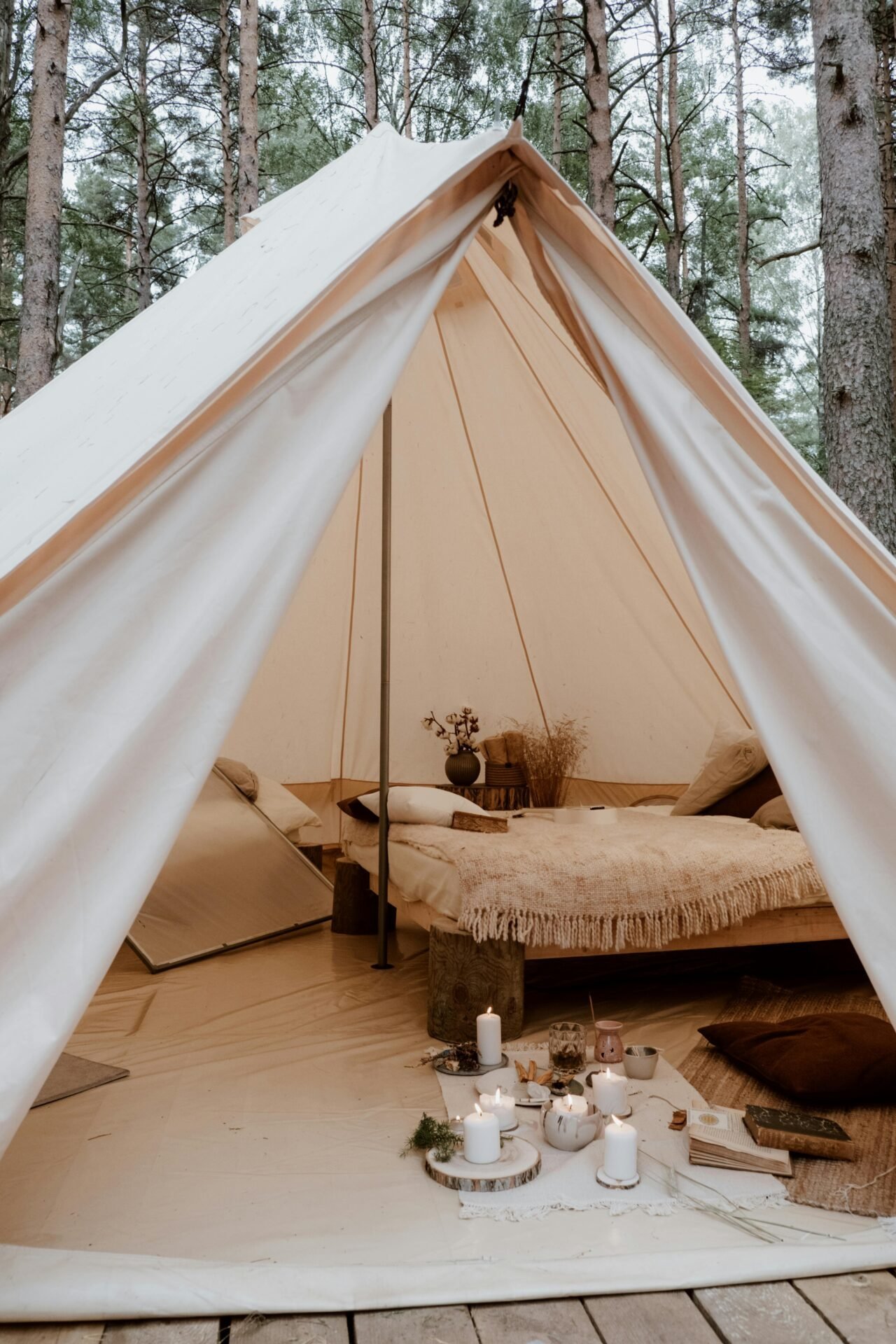 Ein gemütliches Zelt mit Camping-Utensilien, Bett, Kissen, Kerzen und rustikaler Einrichtung in einem Wald.