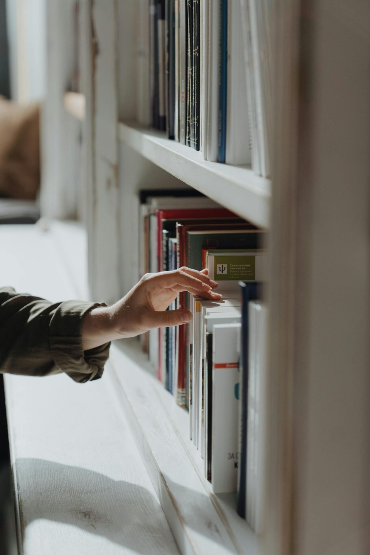 Eine Hand greift nach einem Buch auf einem sonnenbeschienenen Bücherregal, bereit, erfolgreich zu lernen.