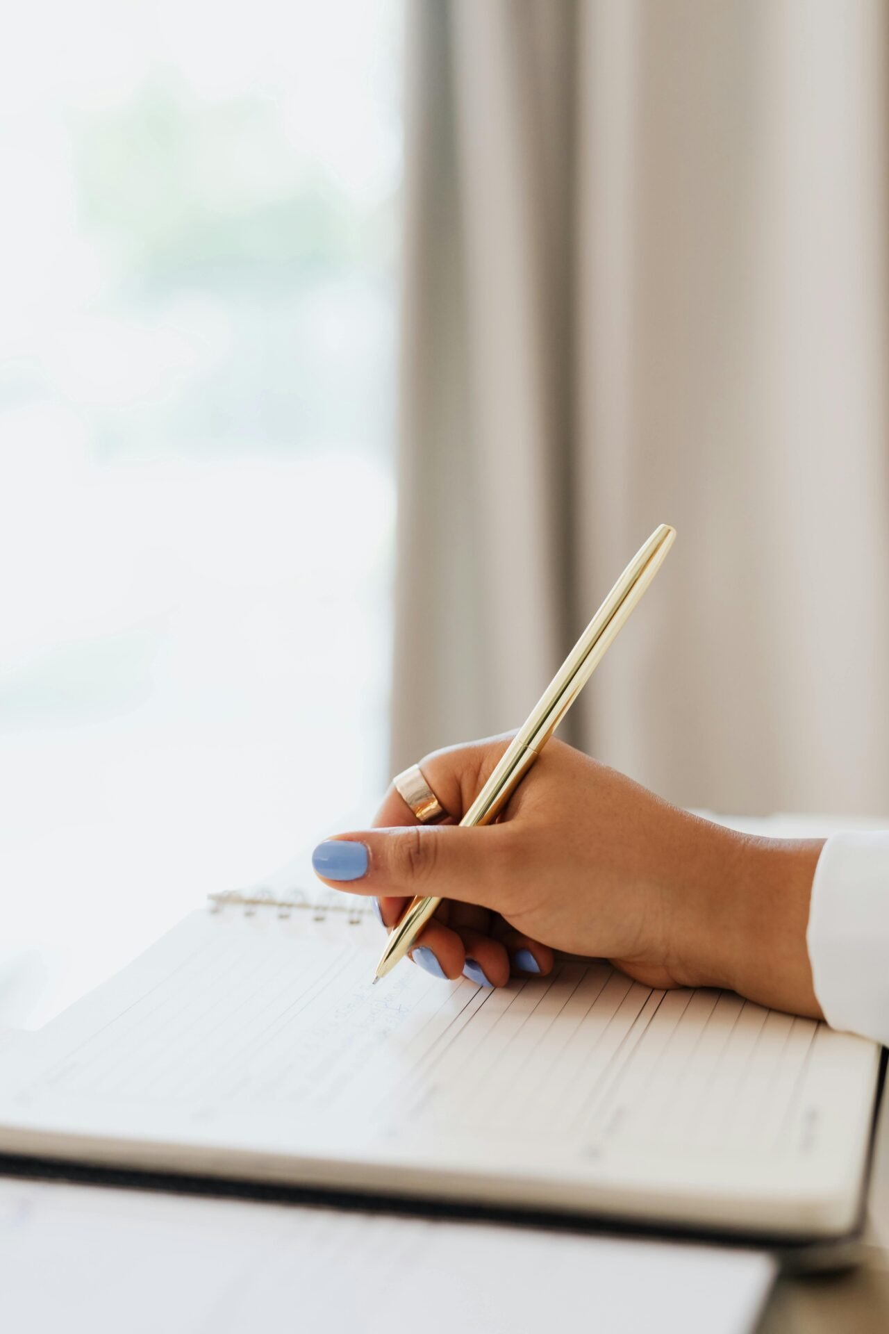 Eine Person mit blauen Nägeln schreibt mit einem goldenen Stift Tipps zum erfolgreichen Lernen in ein liniertes Notizbuch.