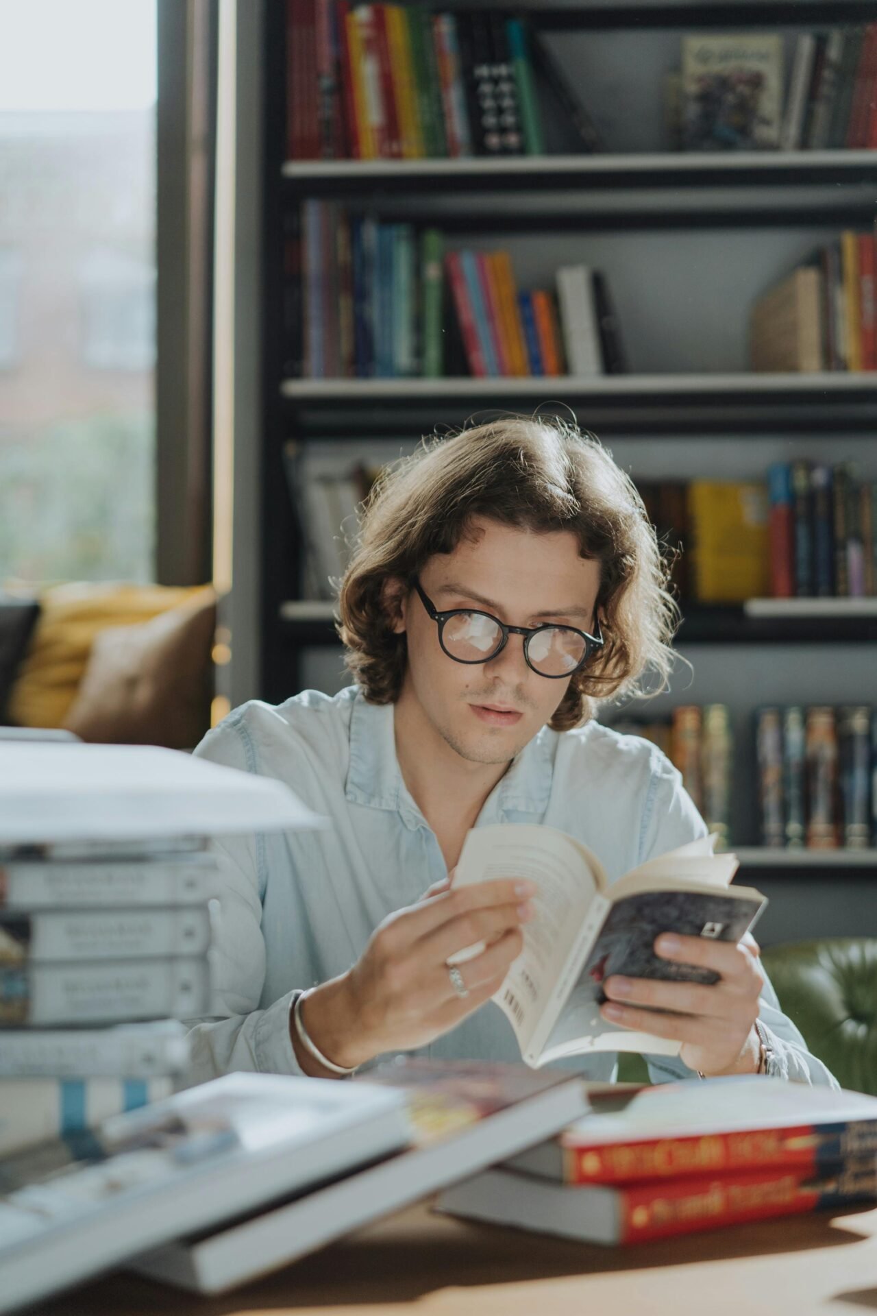 Person mit Brille liest, umgeben von Büchern – erfolgreich lernen in der Bibliothek.