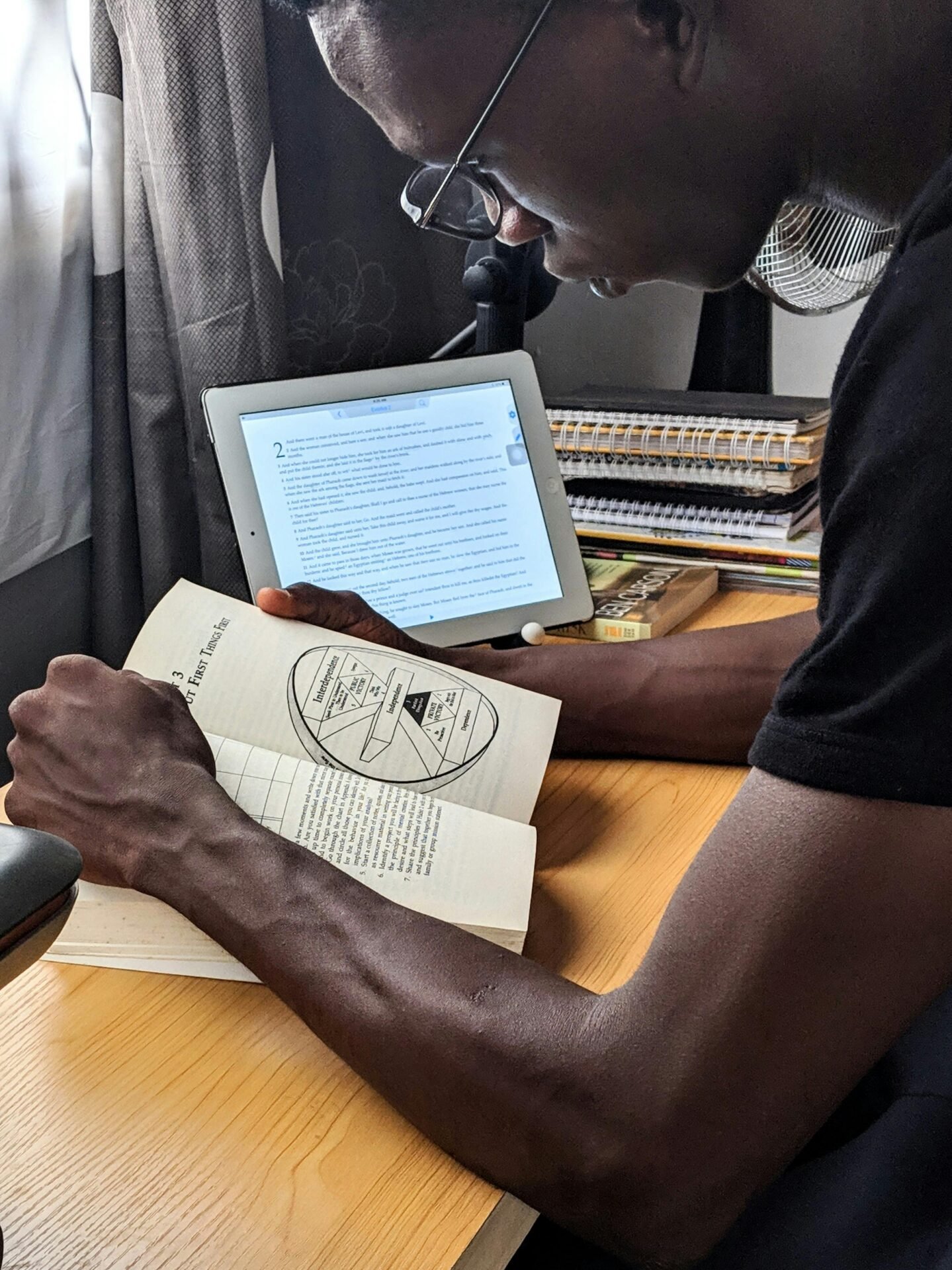 Eine Person liest ein Buch am Schreibtisch, um erfolgreich mit Tablet-Unterstützung zu lernen.