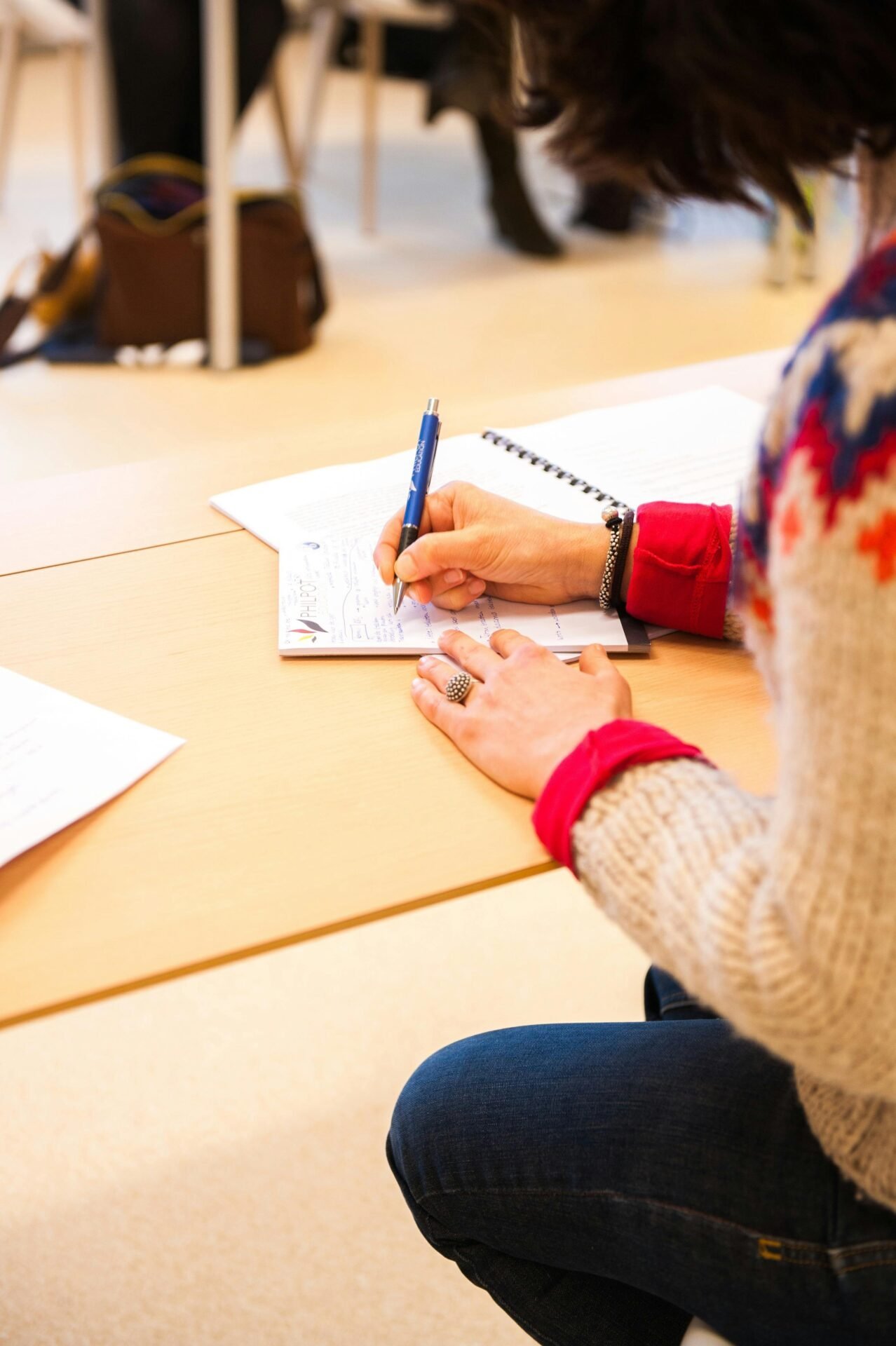 Person am Schreibtisch, schreibt mit blauen Stift Notizen zum erfolgreichen Präsentieren.