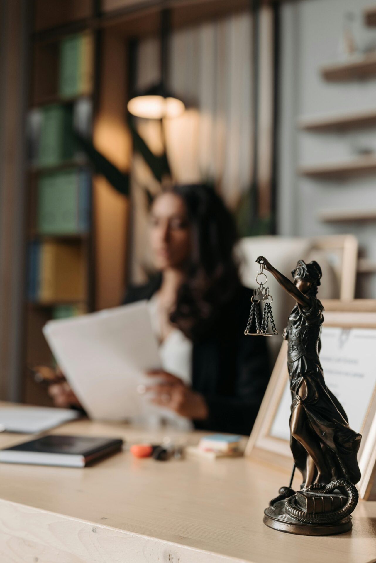 Eine Justitia-Statue auf einem Schreibtisch, im Hintergrund lesen erfolgreiche Frauen Zeitung.