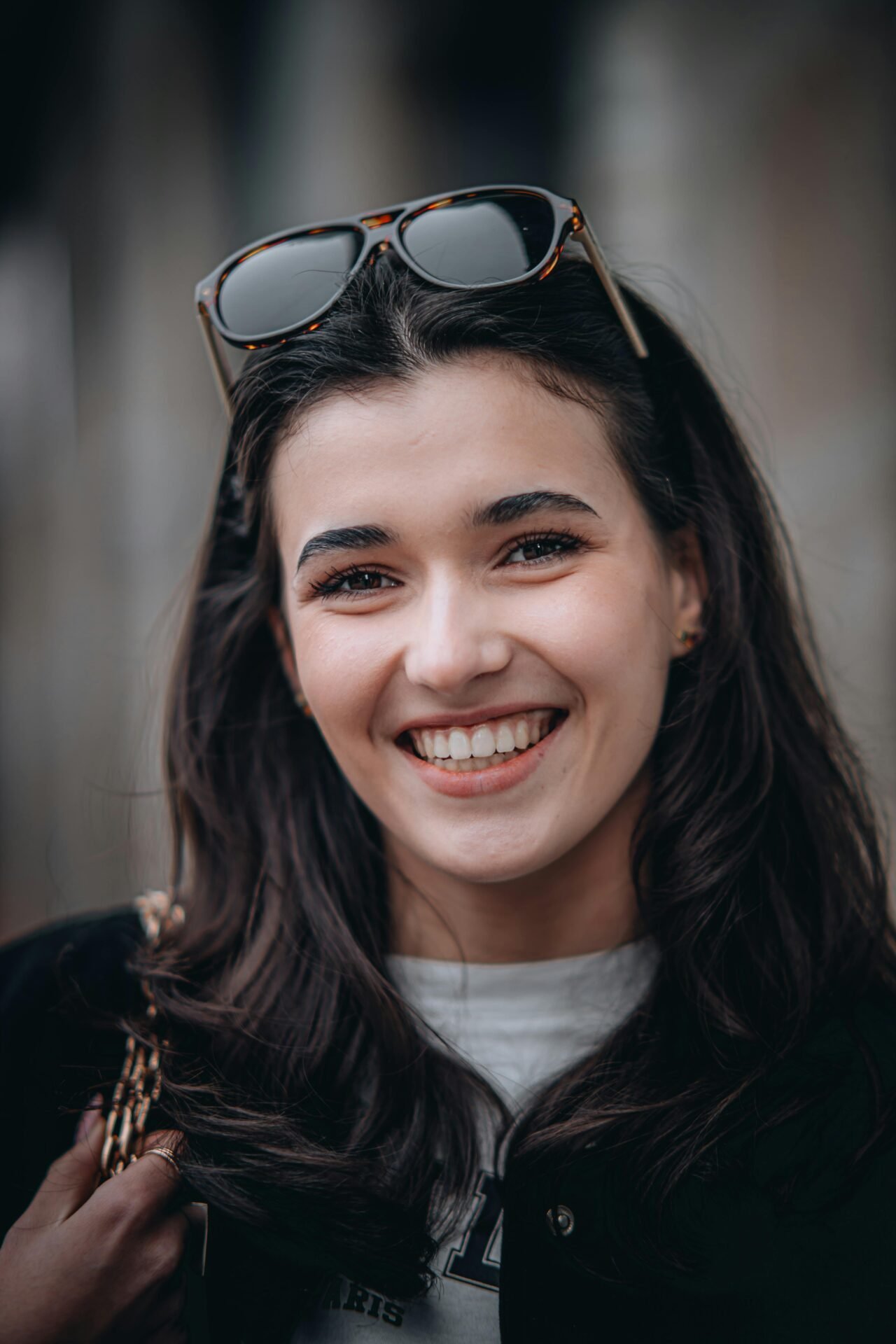 Eine junge Frau mit langen dunklen Haaren, die wie erfolgreiche Menschen lächelt und eine Sonnenbrille auf dem Kopf hat.