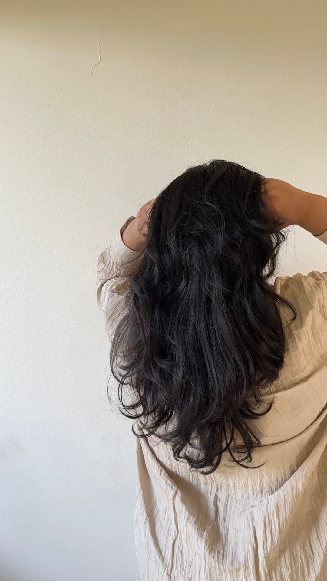 Person mit langen, welligen dunklen Haaren, die in einem beigen Hemd finanzielle Freiheit genießt.