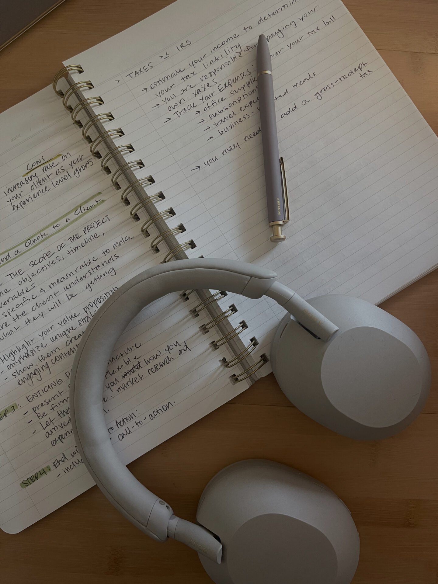 Offenes Notizbuch mit Notizen, Stift und grauen Kopfhörern – planen Sie Ihre finanzielle Freiheit.