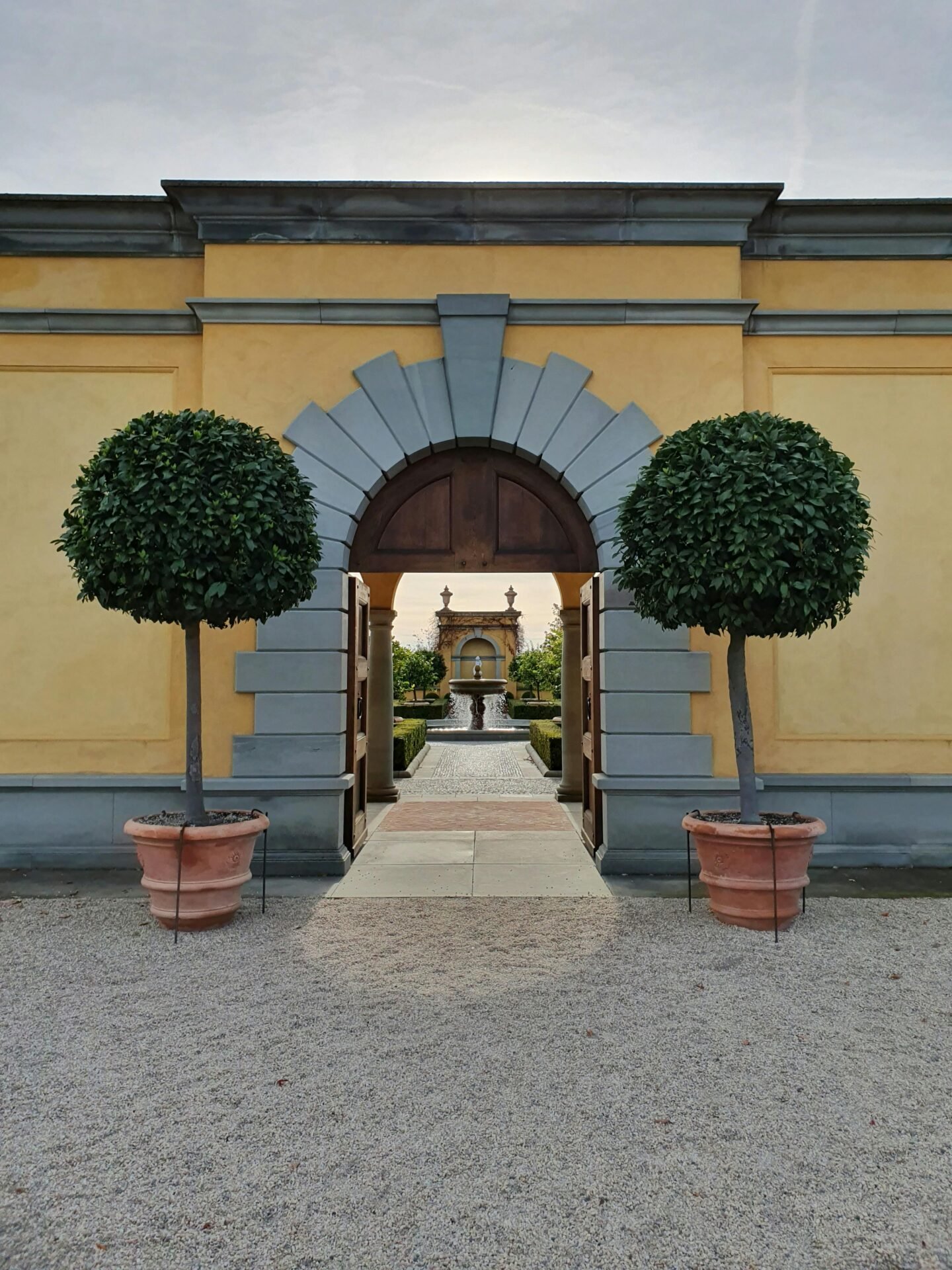 Gelber Torbogen mit getopften Bäumen, die eine Gartenansicht einrahmen - klassischer Berliner Sehenswürdigkeiten-Charme.