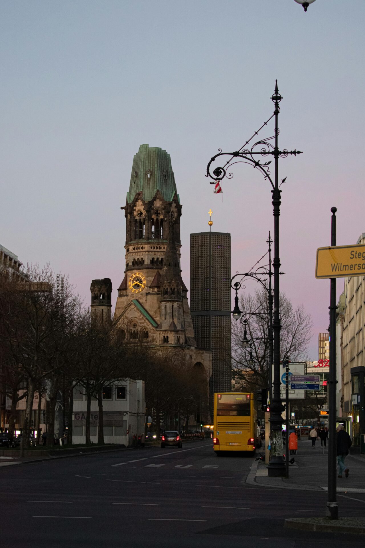 Eine Straßenansicht der Kaiser-Wilhelm-Gedächtniskirche, einer Berliner Sehenswürdigkeit, in der Abenddämmerung.