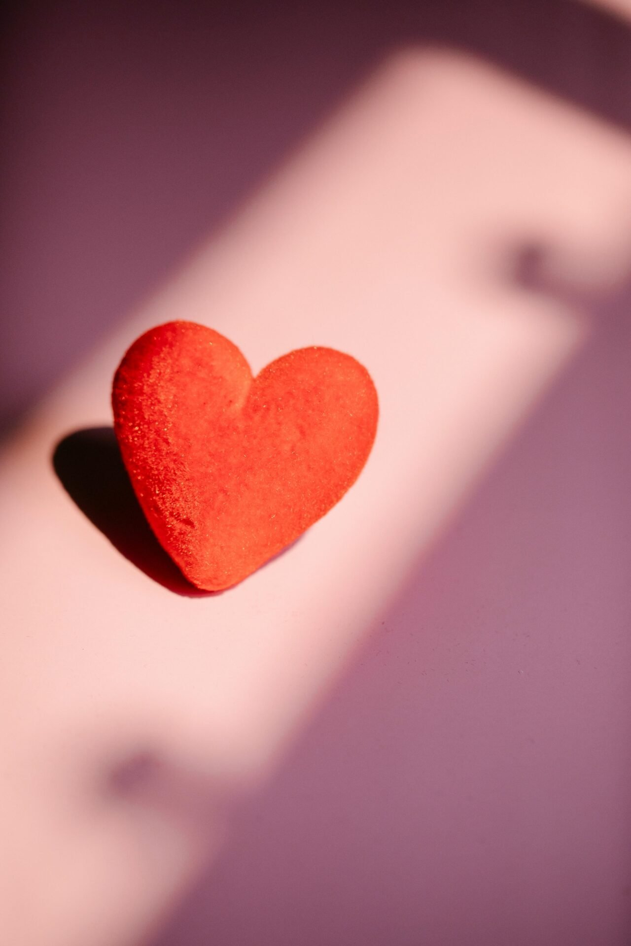 Ein rotes herzförmiges Objekt, das Glück und Gesundheit auf rosa und violettem Hintergrund symbolisiert.