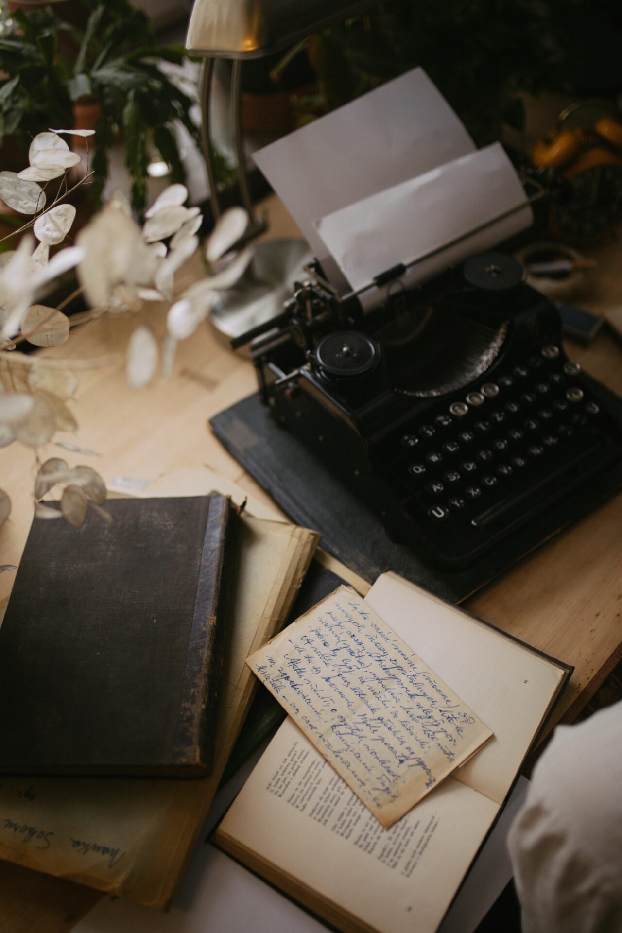 Vintage-Schreibmaschine auf dem Schreibtisch mit Büchern, Papieren und einem handgeschriebenen Glück-Zitate-Kurz-Brief in der Nähe.