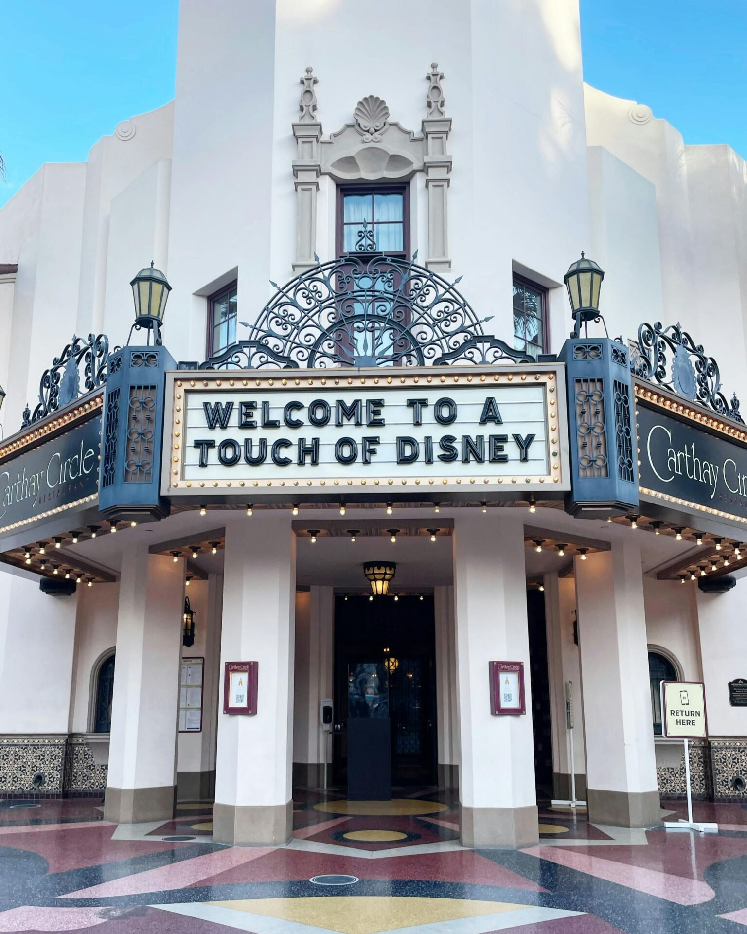 Eingang zum Carthay Circle mit einem Schild mit der Aufschrift „Glück, Zitat, kurz: Willkommen bei einem Hauch von Disney.“.