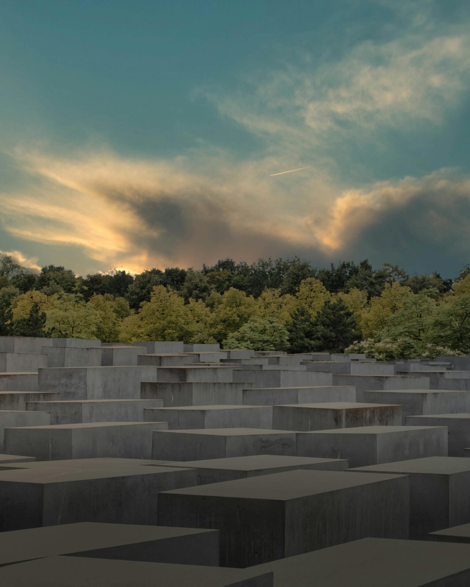 Graue Betonblöcke mit Bäumen dahinter, eine Berliner Sehenswürdigkeit bei Sonnenuntergang.