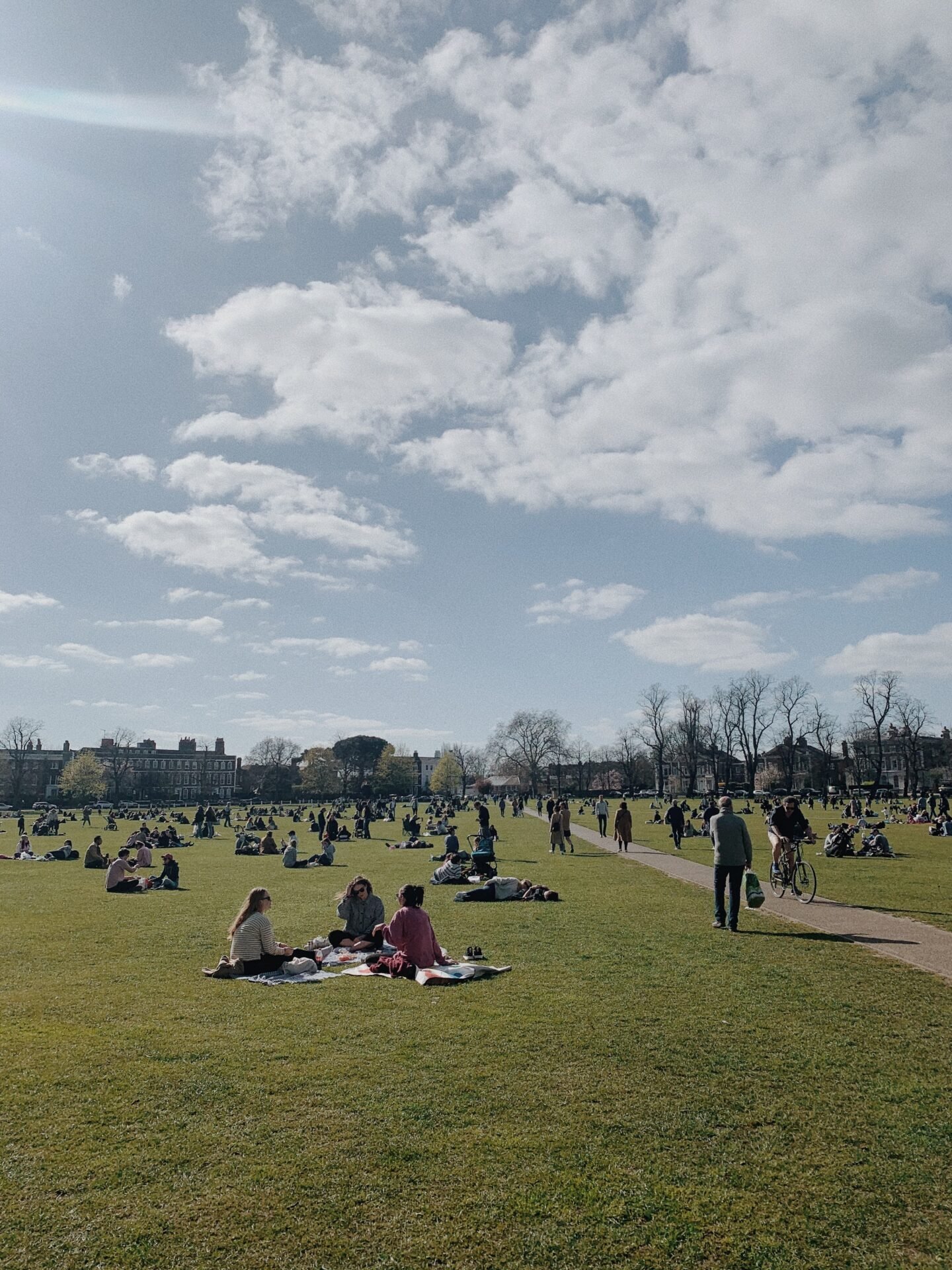 Menschen, die sich auf einer großen Wiese in einem Londoner Park unter einem teilweise bewölkten Himmel entspannen und picknicken.