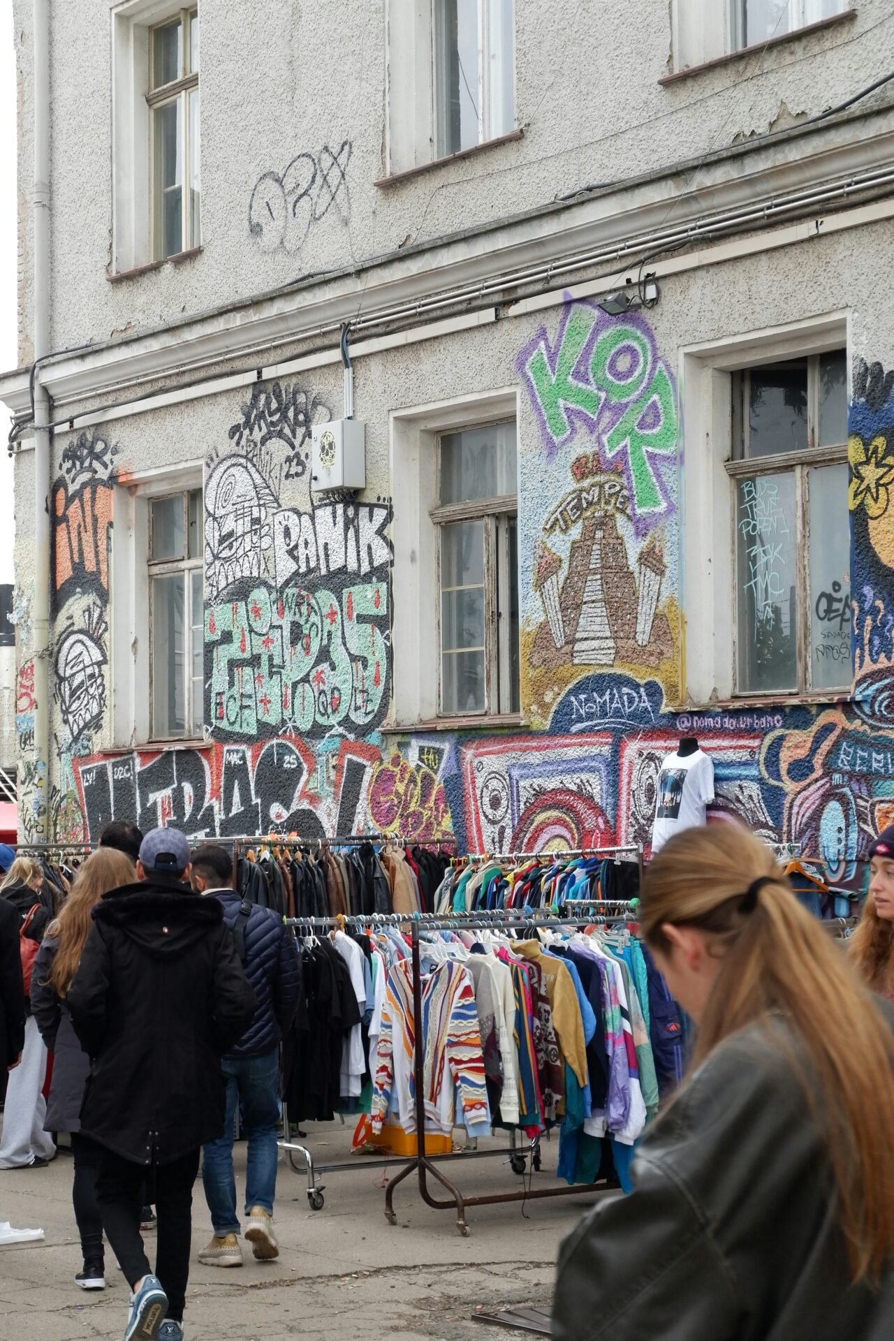 Ein Markt im Freien mit Menschen, die in den Kleiderständern in der Nähe der pulsierenden Berliner Sehenswürdigkeiten und Graffiti stöbern.