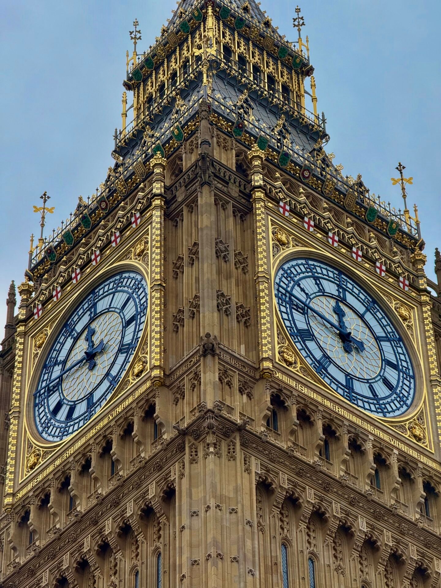 Nahaufnahme des Uhrenturms Big Ben in London mit zwei großen Zifferblättern vor einem bewölkten Himmel.