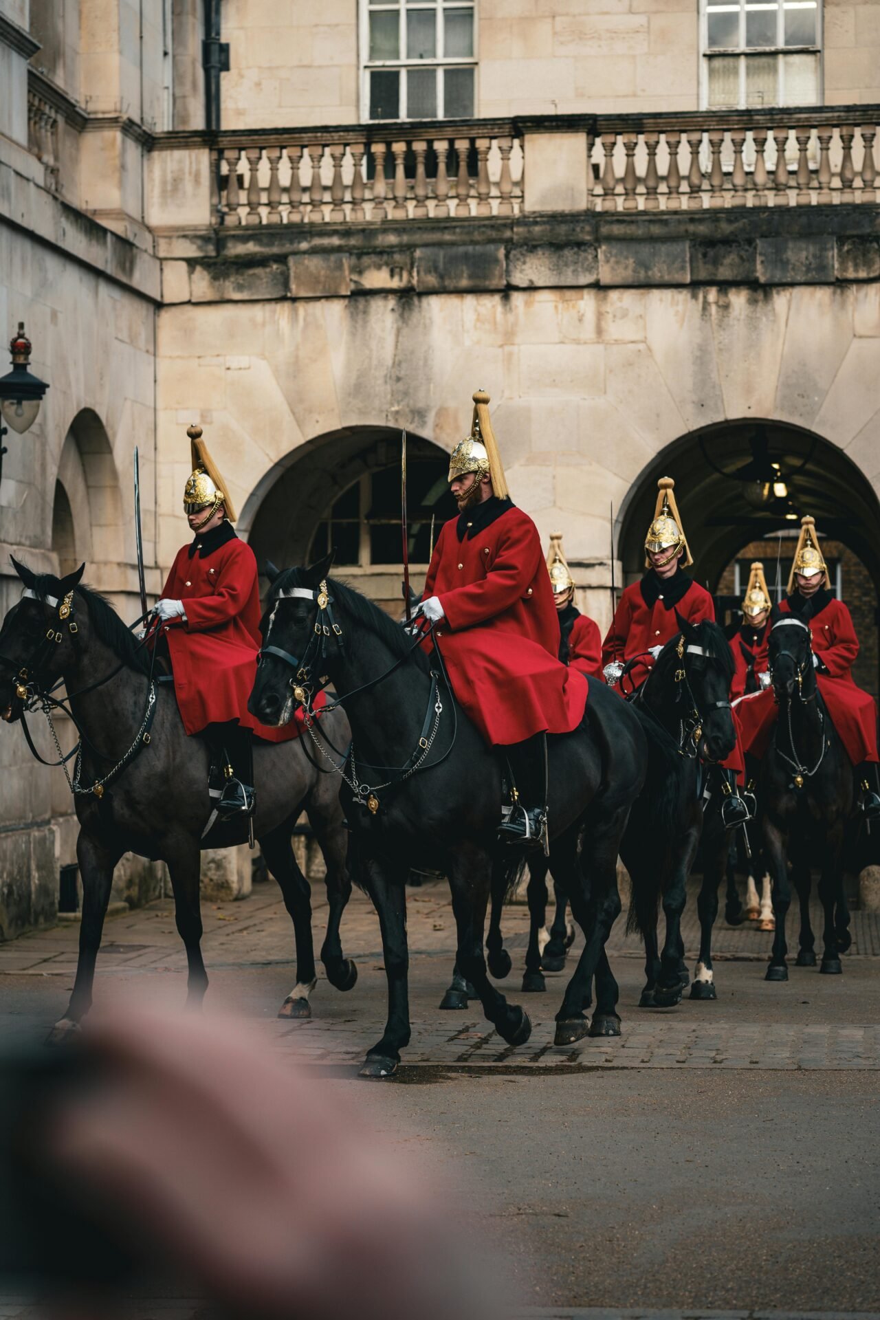 Eine Gruppe von Wachleuten in roten Uniformen reitet auf schwarzen Pferden in der Nähe eines steinernen Gebäudes in London.