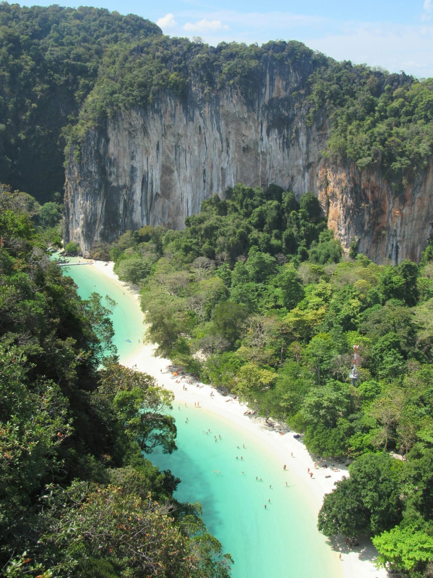 Eine türkisfarbene Lagune mit Sandstrand, umgeben von üppigen Klippen und einem Mai-Pen-Rai-Wald.