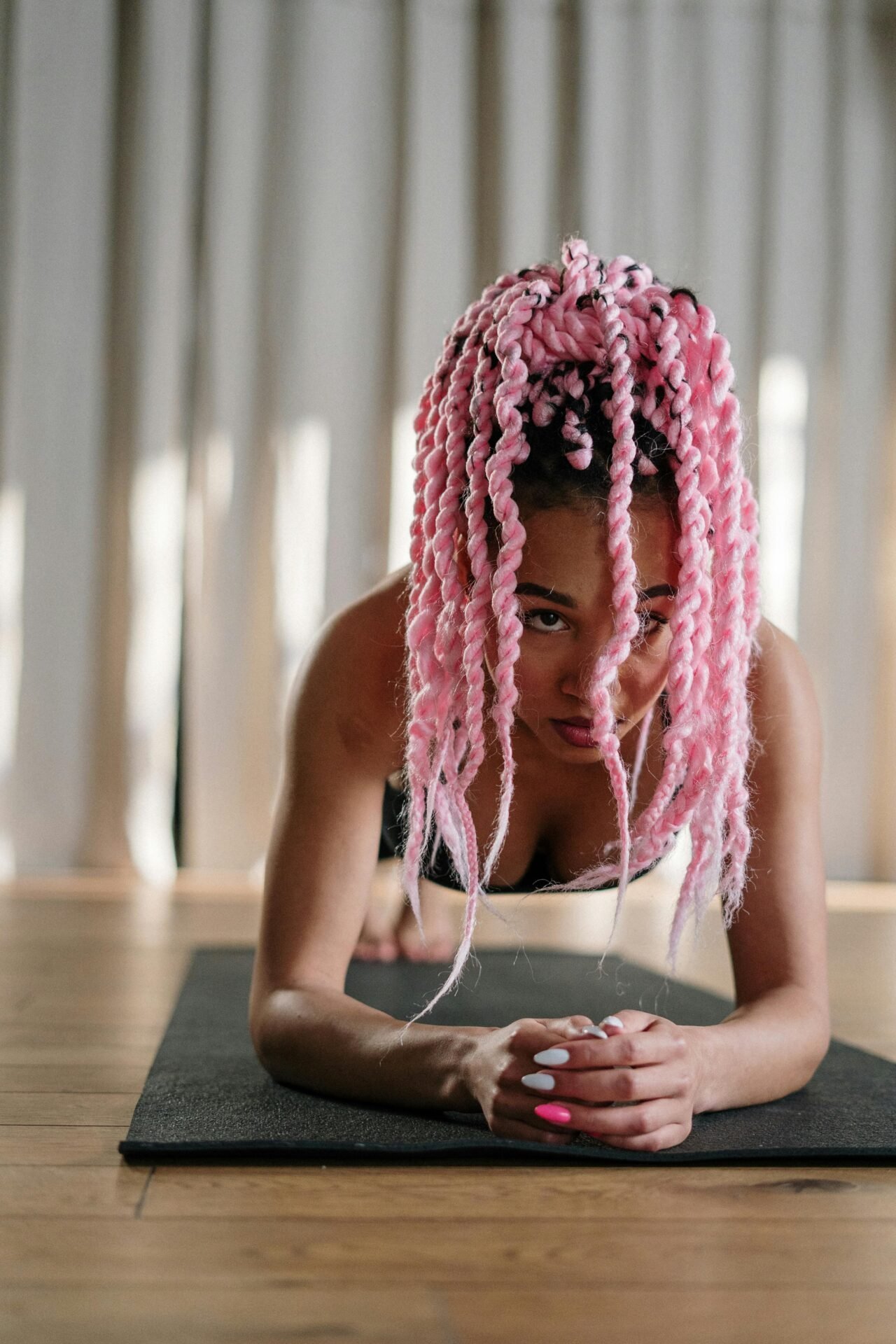 Frau mit rosa Zöpfen macht eine Plank-Übung und nimmt sich drinnen auf ihrer Yogamatte einen Mentalwechsel vor.