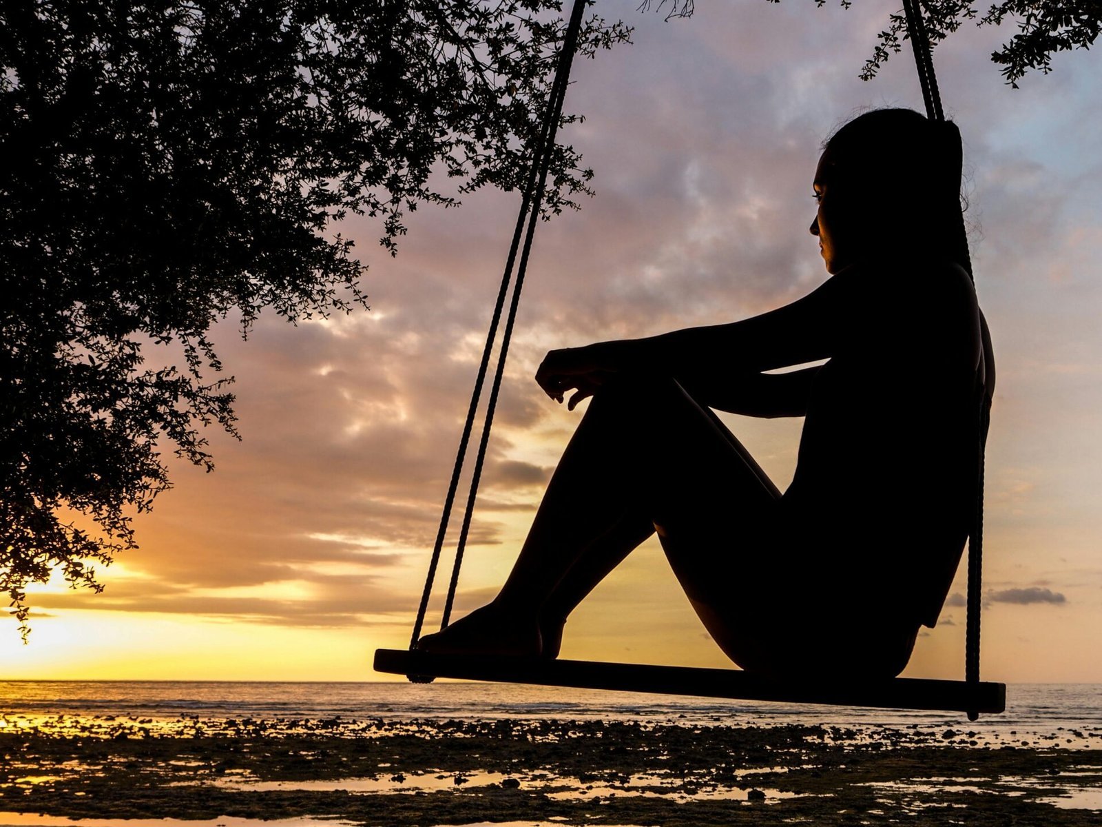 Silhouette einer Person, die bei Sonnenuntergang auf einer Schaukel am Strand sitzt und dabei ihre Denkweise ändert.