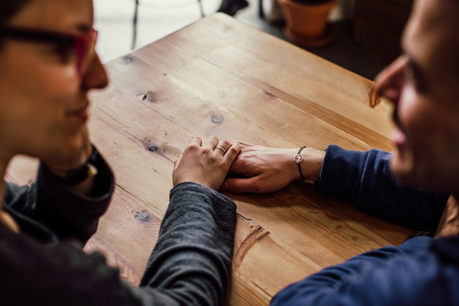 Zwei Menschen sitzen an einem Tisch und halten sich sanft an den Händen – ein ruhiger Moment, um gemeinsam die Denkweise zu ändern.