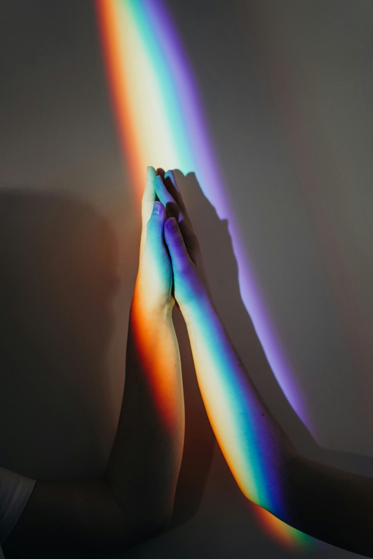 Zwei Hände berühren sich, während ein Regenbogenlicht bunte Schatten wirft und so eine Änderung der Denkweise symbolisiert.