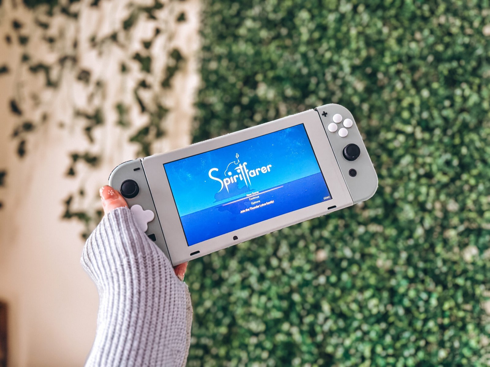 Hand hält einen Nintendo Switch mit Spiritfarer, perfekt für Ausfallzeiten im Online-Geschäft, grüner Hintergrund.