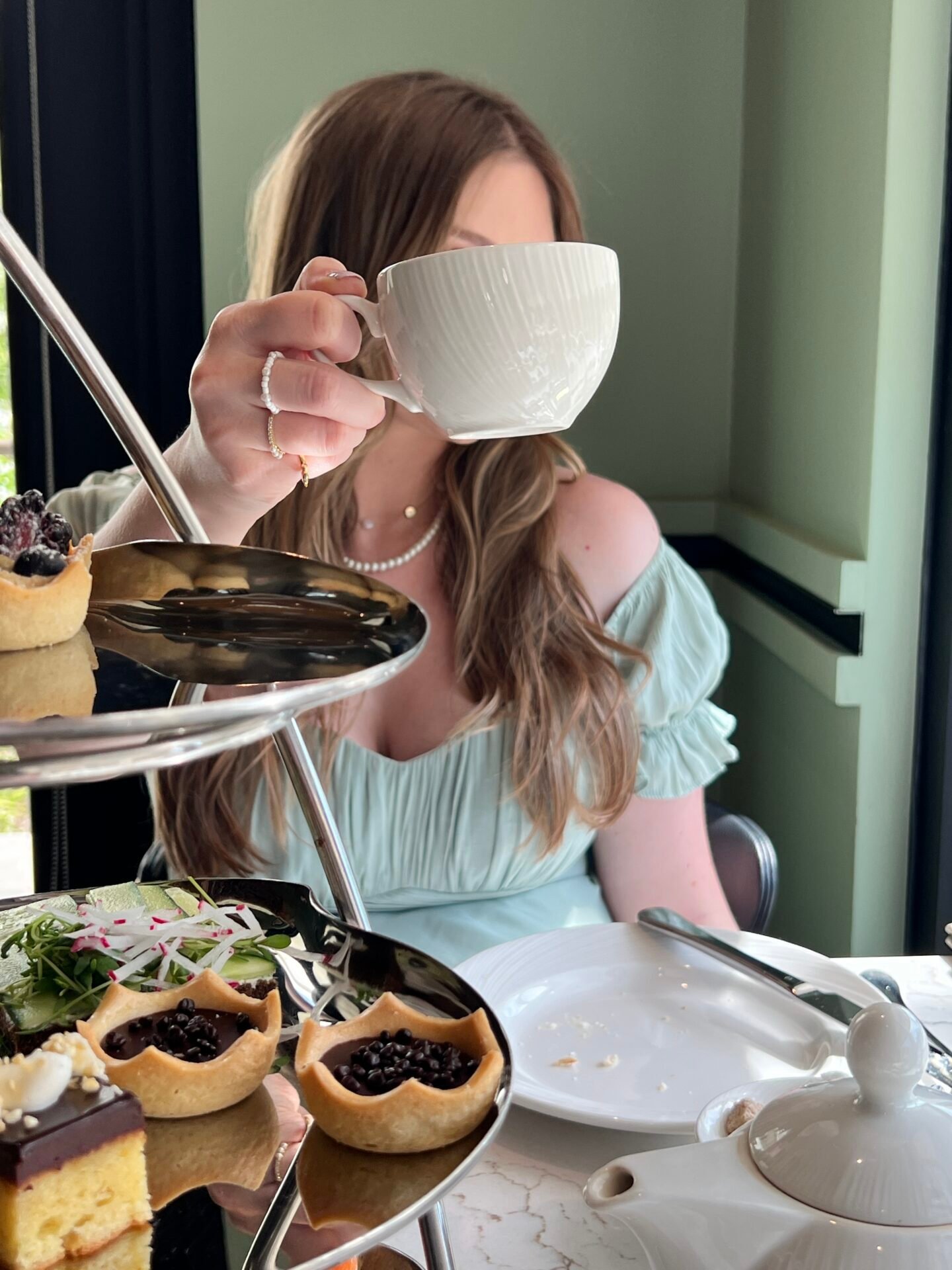 Eine Frau in einem leichten Kleid hält eine Teetasse mit Gebäck und Tee an ihrem Online-Geschäftstisch.