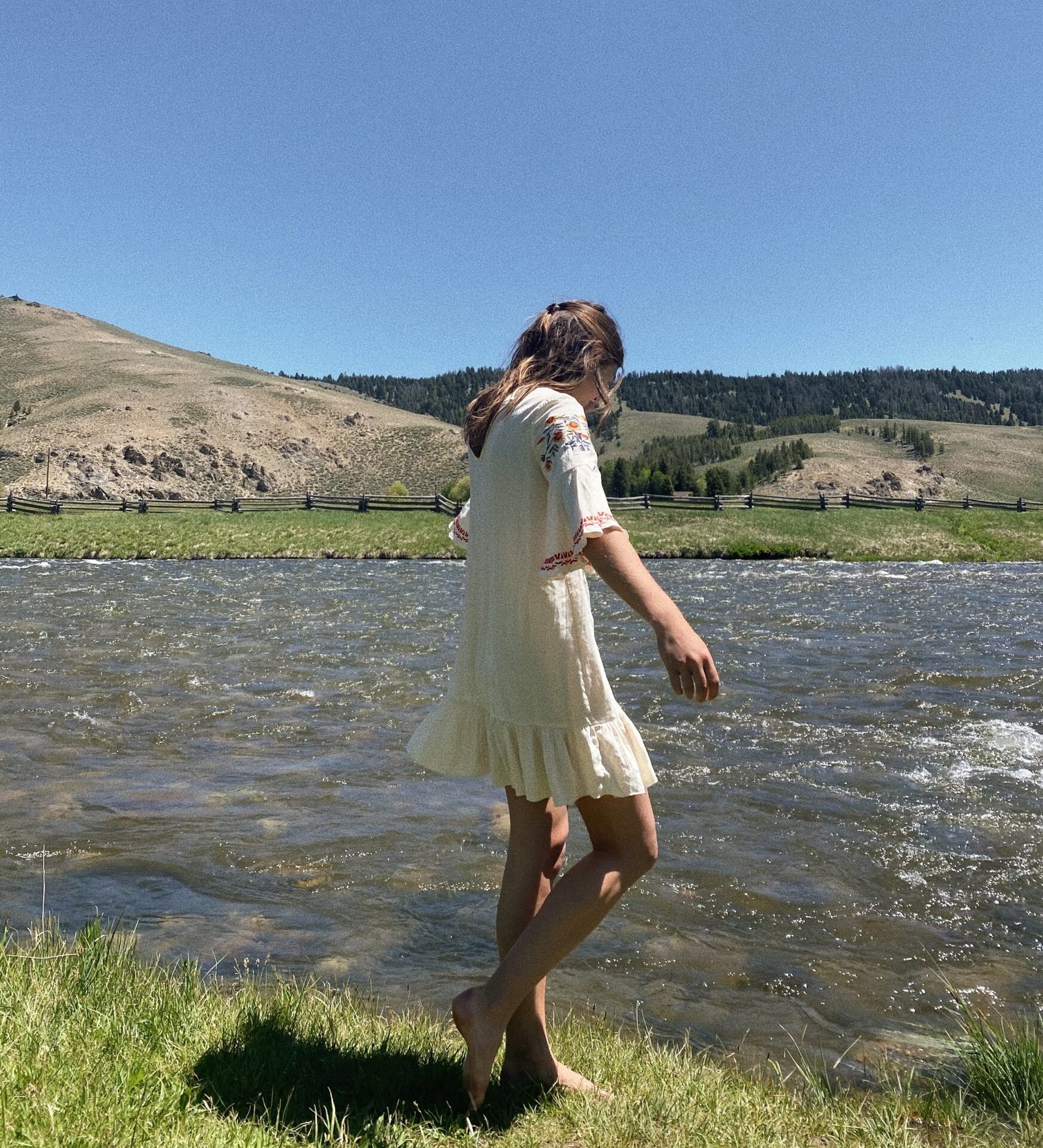 Ein Mädchen in einem weißen Kleid schlendert barfuß an einem Fluss entlang und träumt von ihrem zukünftigen Online-Geschäft.