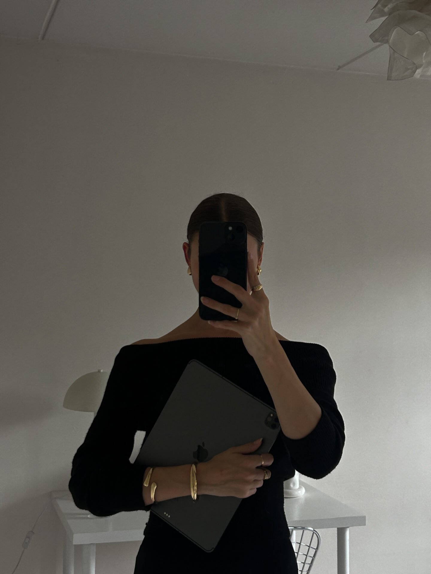 Person in schwarzem Outfit macht ein Spiegel-Selfie und hält ein Tablet – minimalistisches Weiß, Online-Business-Atmosphäre.