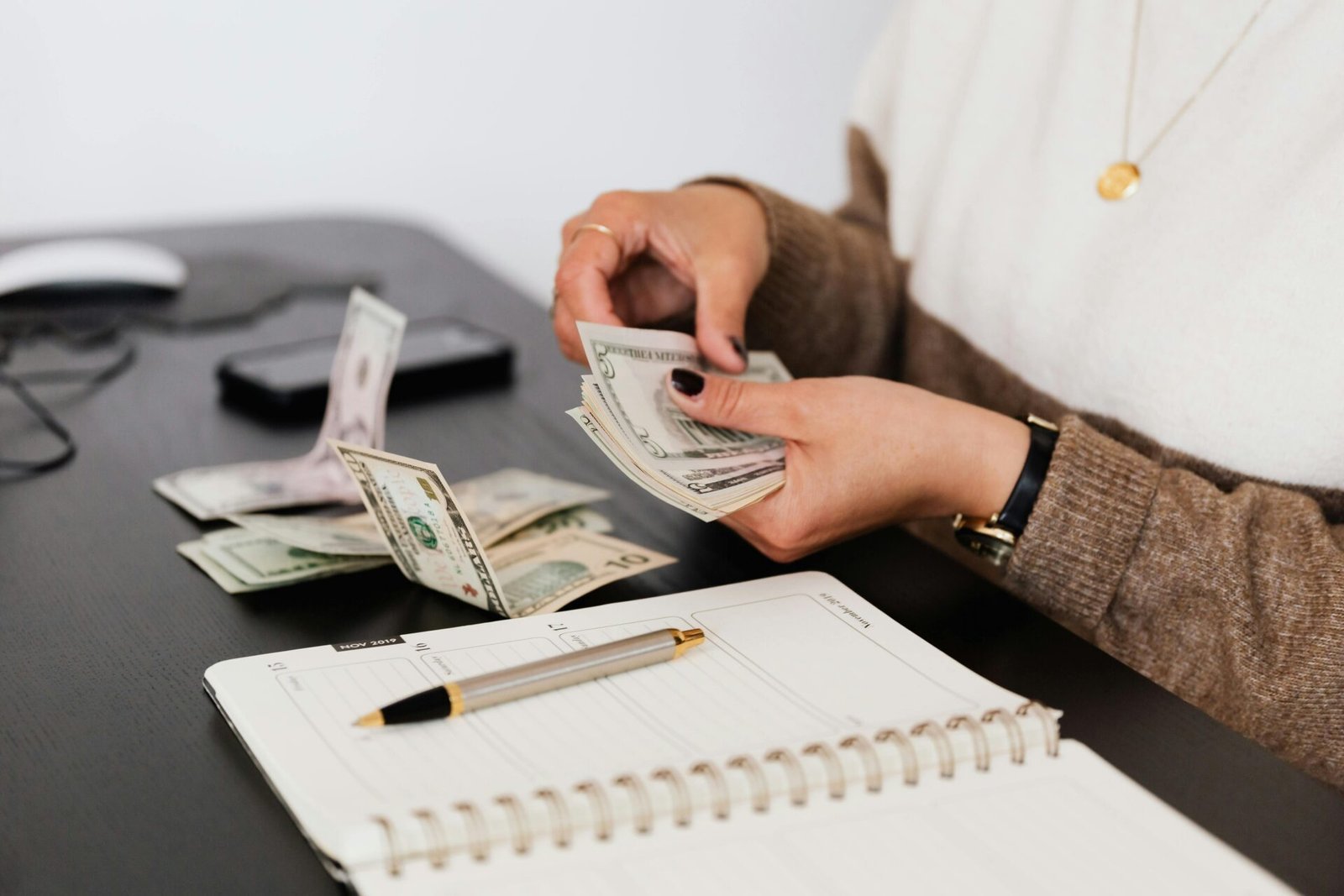 Person zählt Dollarscheine an einem Schreibtisch – verwaltet den Cashflow für ein Online-Geschäft.