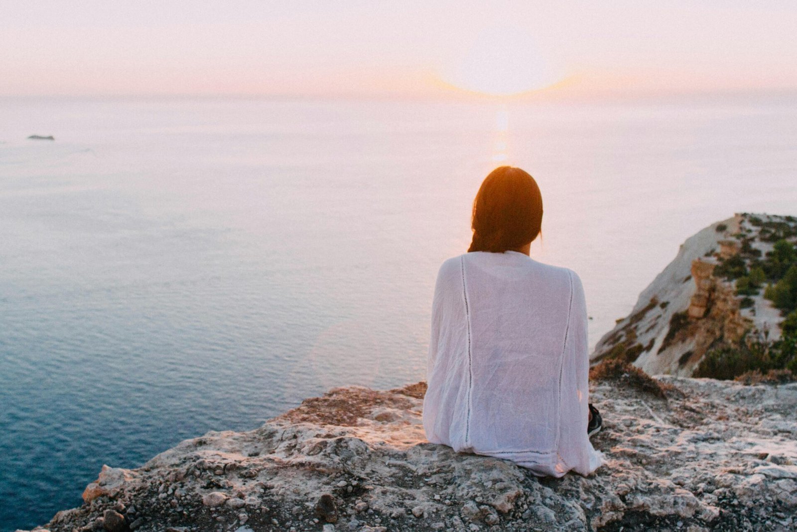 Person, die auf einer Klippe sitzt und bei Sonnenuntergang am Meer von ihrem nächsten Online-Geschäft träumt.