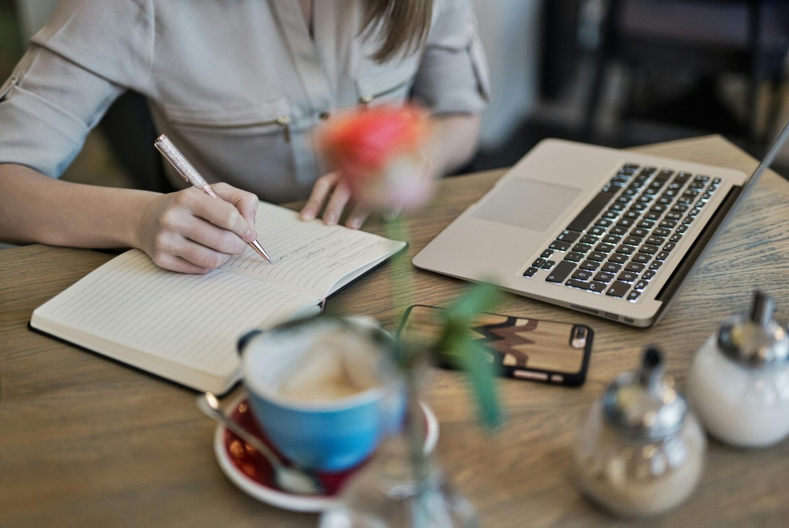 Person, die ihr Online-Geschäft in einem Notizbuch neben Laptop, Telefon und Kaffee plant.