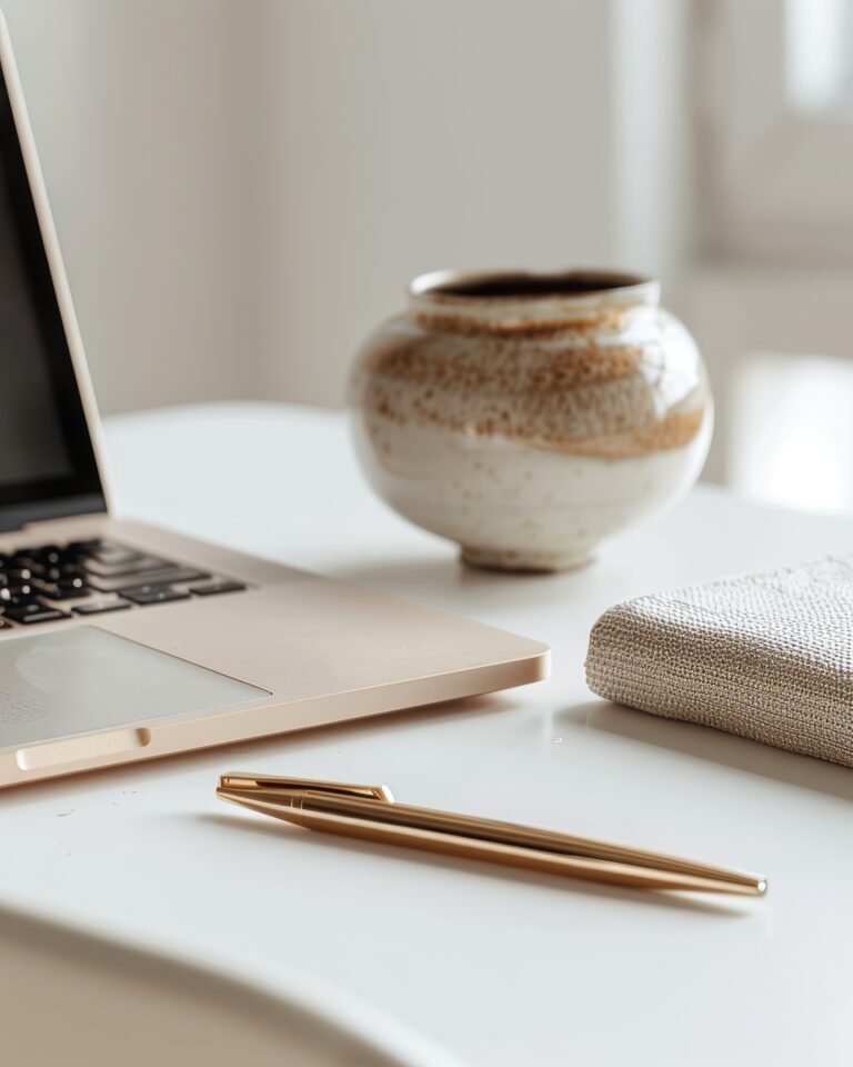 Goldene Stifte, ein geschlossener Laptop und ein strukturiertes Notizbuch für Ihr Online-Geschäft auf einem weißen Schreibtisch.
