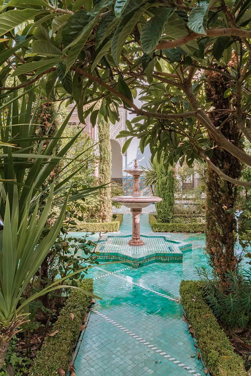 Brunnen in einem üppigen Pariser Garten mit grünen Kacheln und Laubbäumen, die die Aussicht einrahmen.