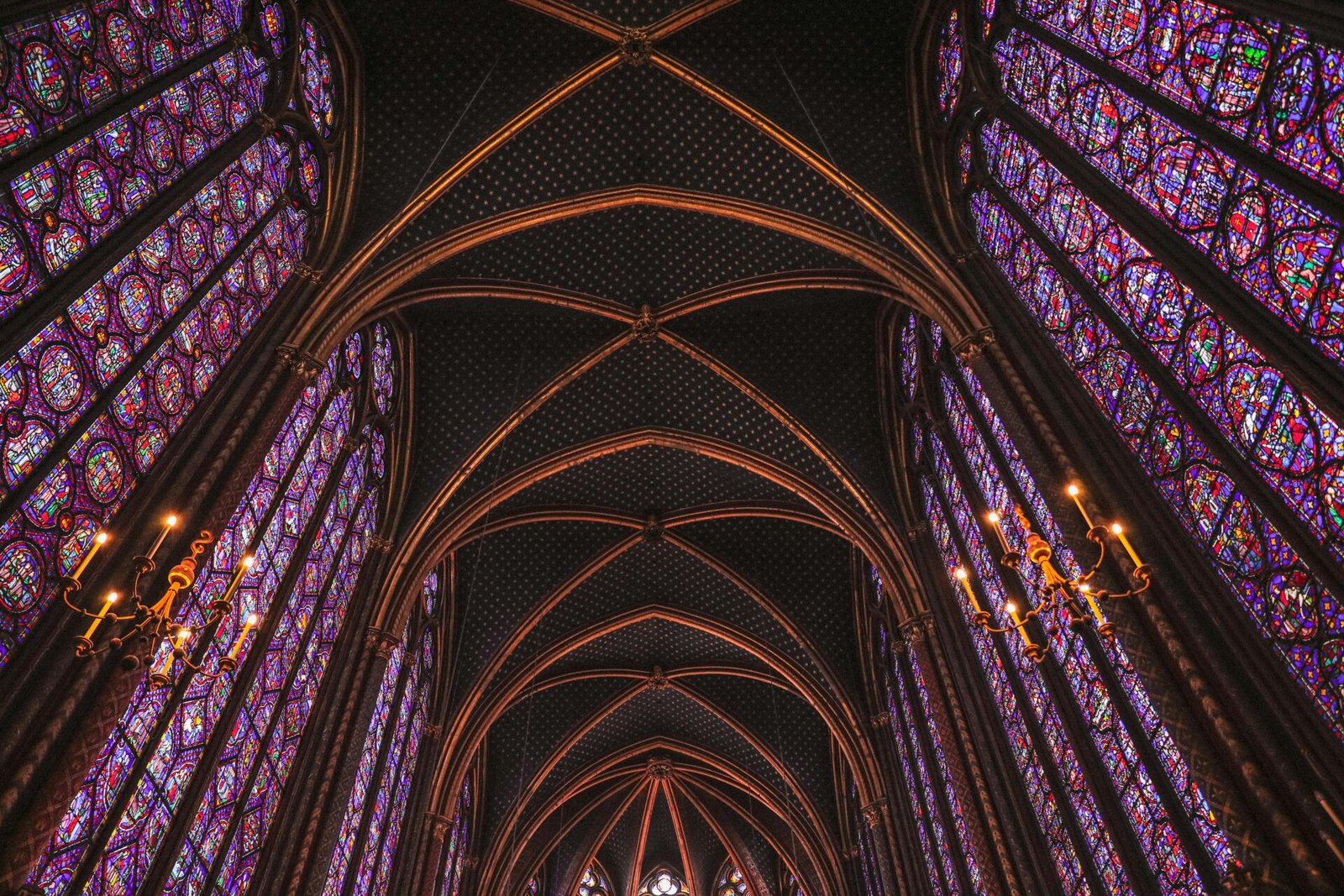 Gotische Glasfenster und kunstvolle Gewölbedecken in einer Pariser Kathedrale, von unten gesehen.