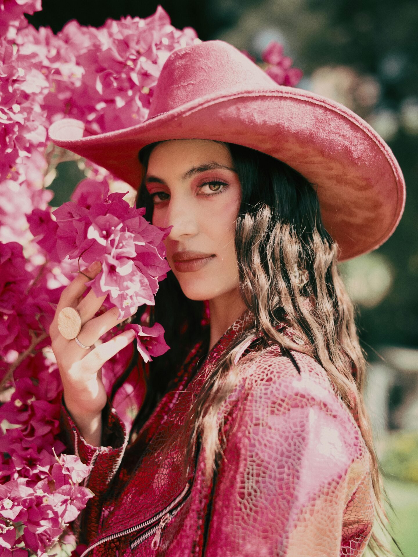 Eine selbstbewusste Frau ganz in Pink riecht an pinken Blumen. Sie trägt einen pinken Cowboyhut, eine piknke Lederjacke und pinkes Make Up. Sie zeigt, dass das Finden eines Lebensziels Selbstbewusstsein erfordert.