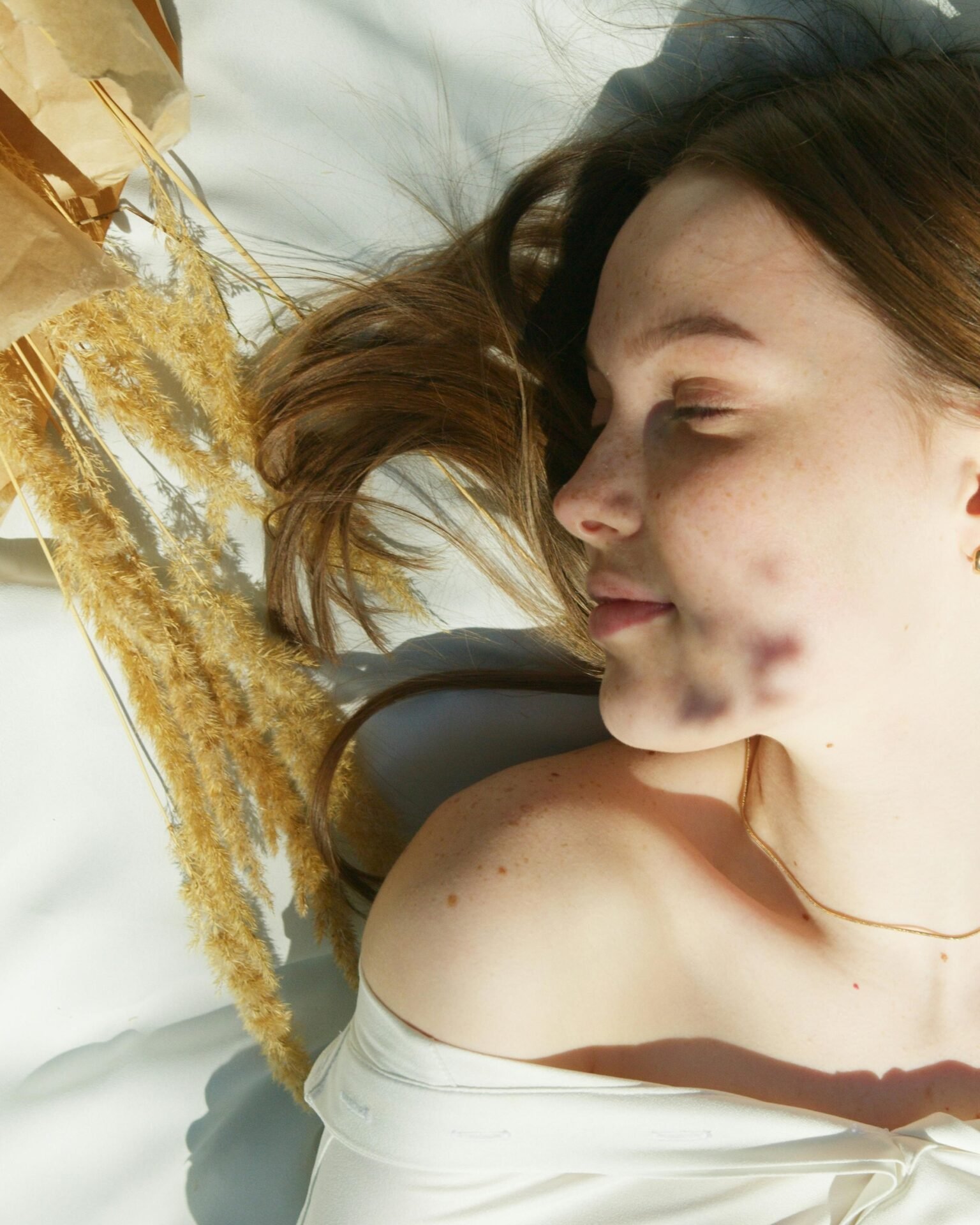 Eine blonde Frau mit geschlossenen Augen auf einer Decke in der Sonne, neben ihr goldene Ähren – ein Moment der Selbstreflexion und inneren Ruhe.