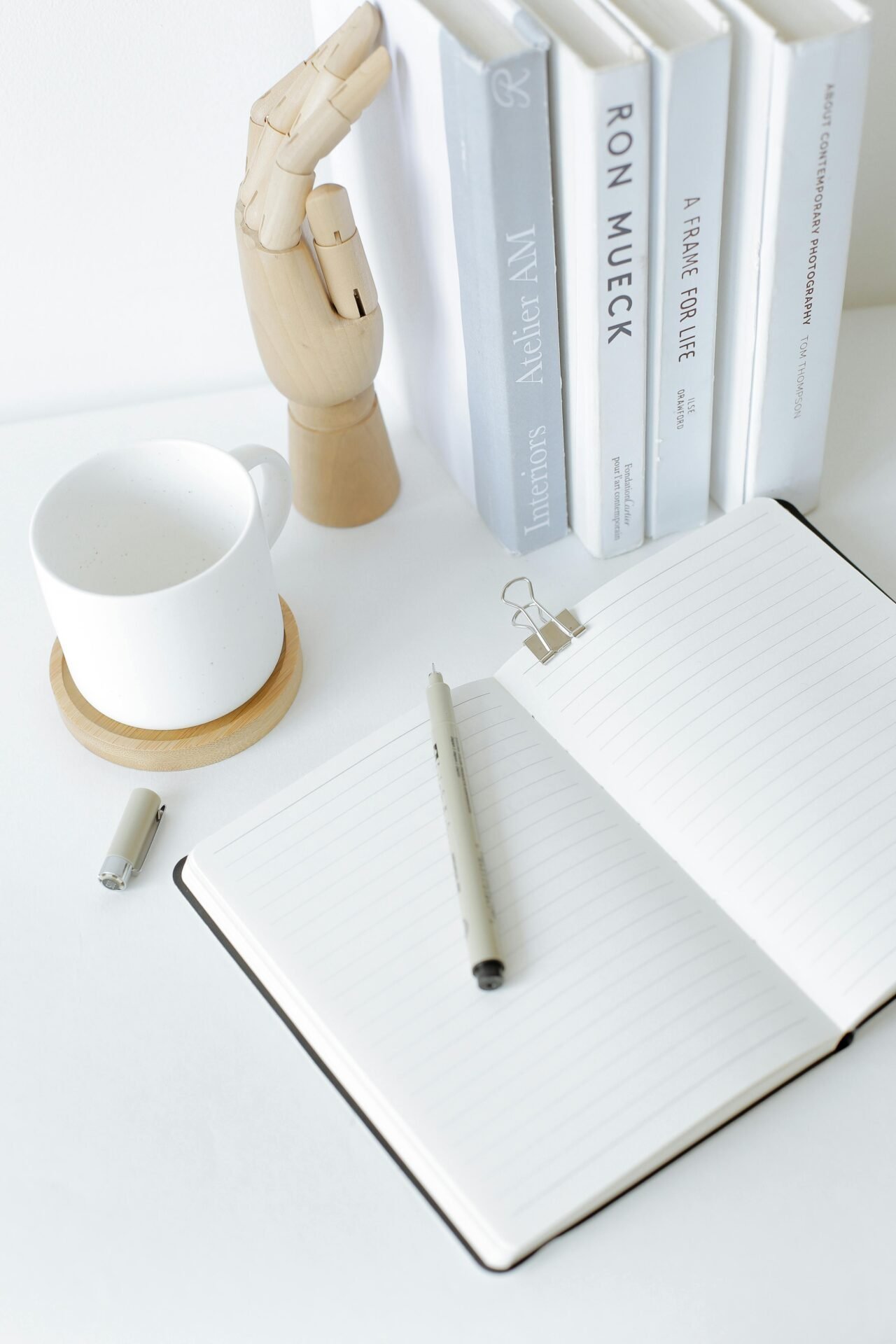 Offenes Notizbuch, Stift und Bücher auf einem weißen Schreibtisch laden zu Glücksmomenten der Inspiration ein.