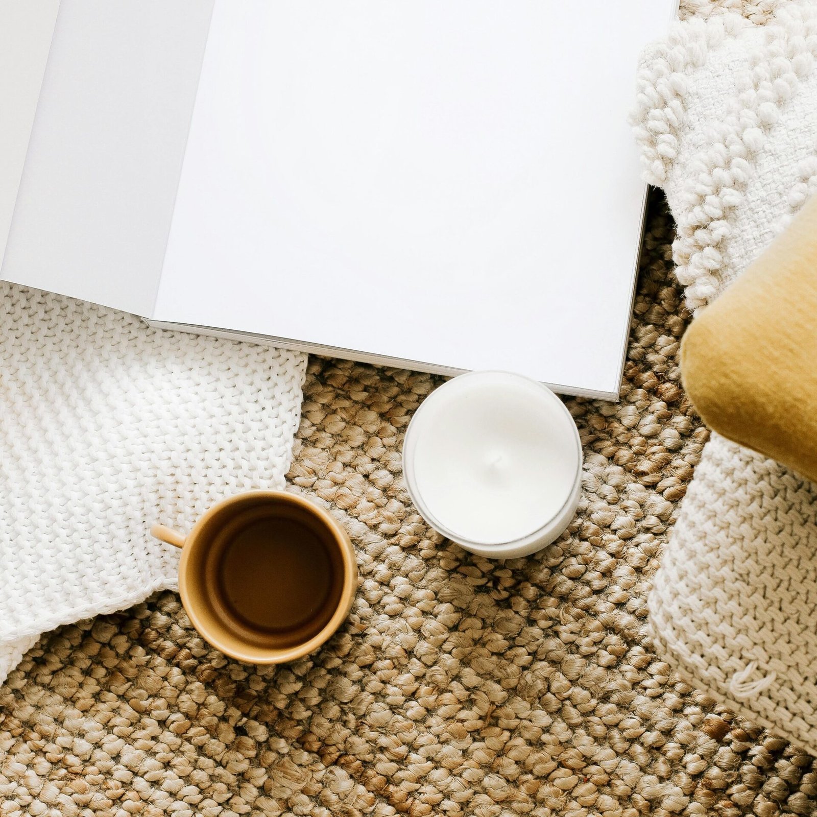 Eine Tasse Kaffee, eine brennende Kerze und ein aufgeschlagenes Buch liegen auf einer Bast-Matte.