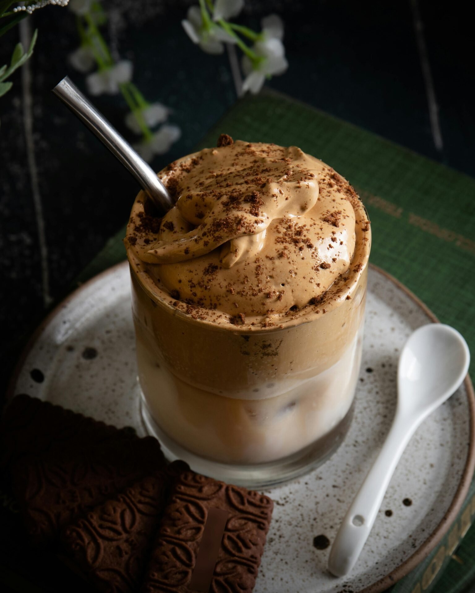 Ein Glas mit einem Kaffeegetränk mit viel Sahne und Kekskrümeln. Daneben liegt ein Löffel und Schokoladenkekse.