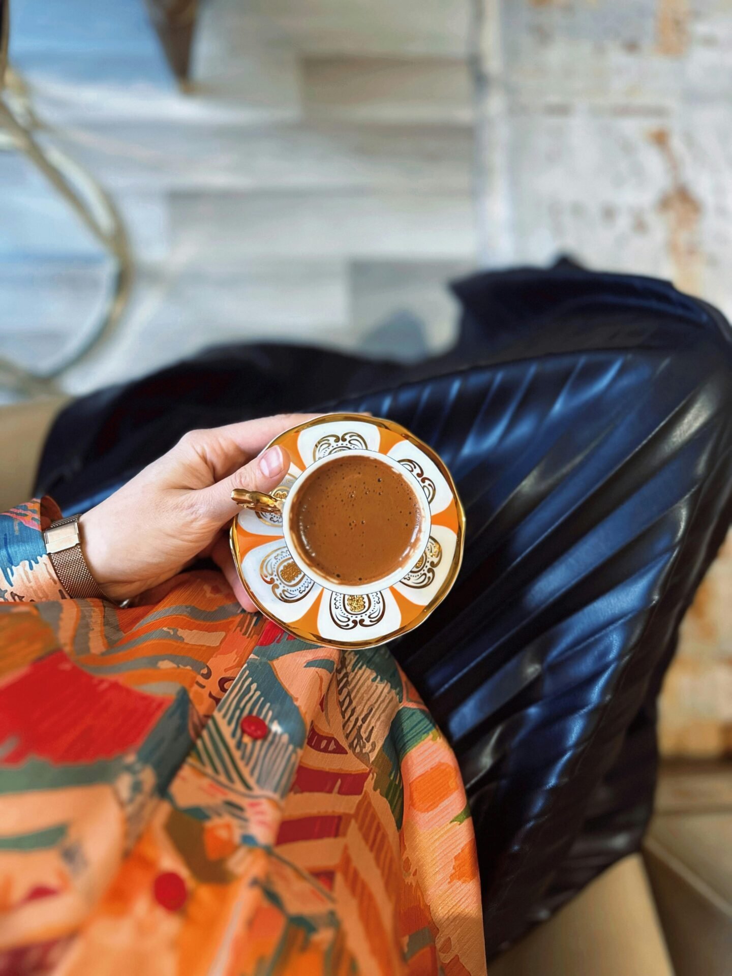 Eine Hand, die Kaffee in einer gemusterten Untertasse hält, ein Faltenrock – perfekt für gesunde Pausen im Leben.