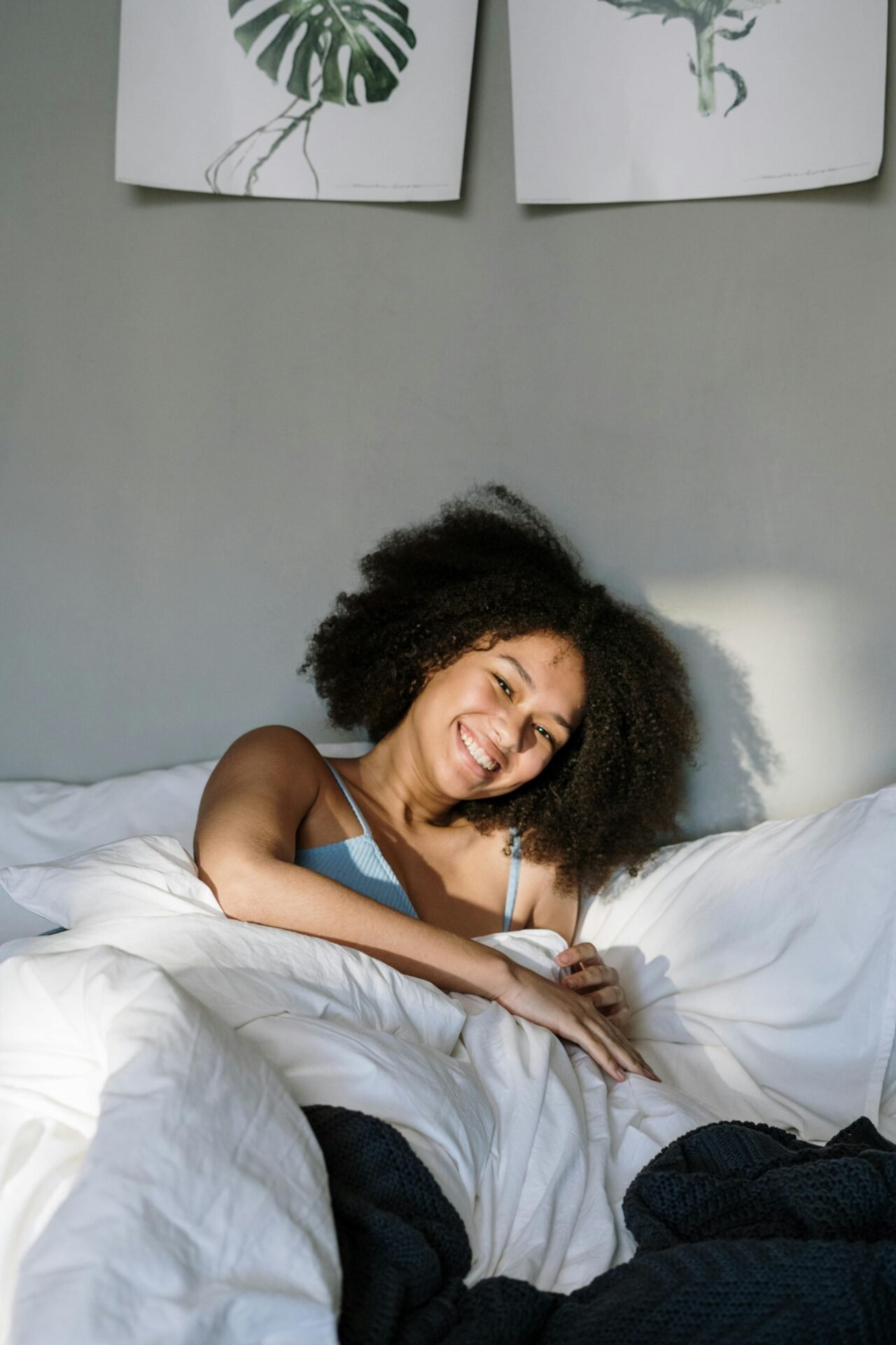 Eine Frau mit einem Afro liegt lachend im Bett.